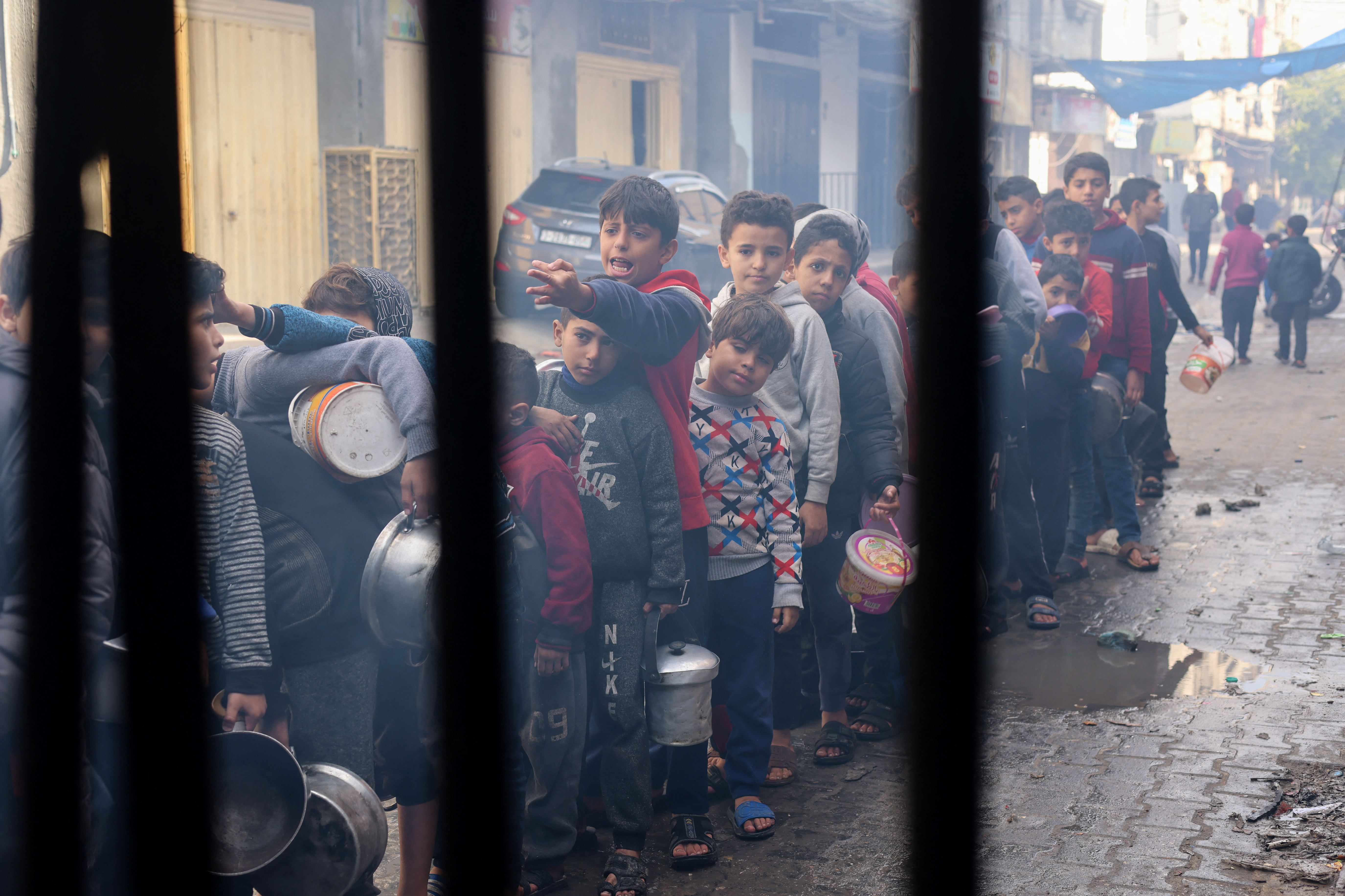 Palestinian children wait to receive food cooked by a charity kitchen, in Rafah