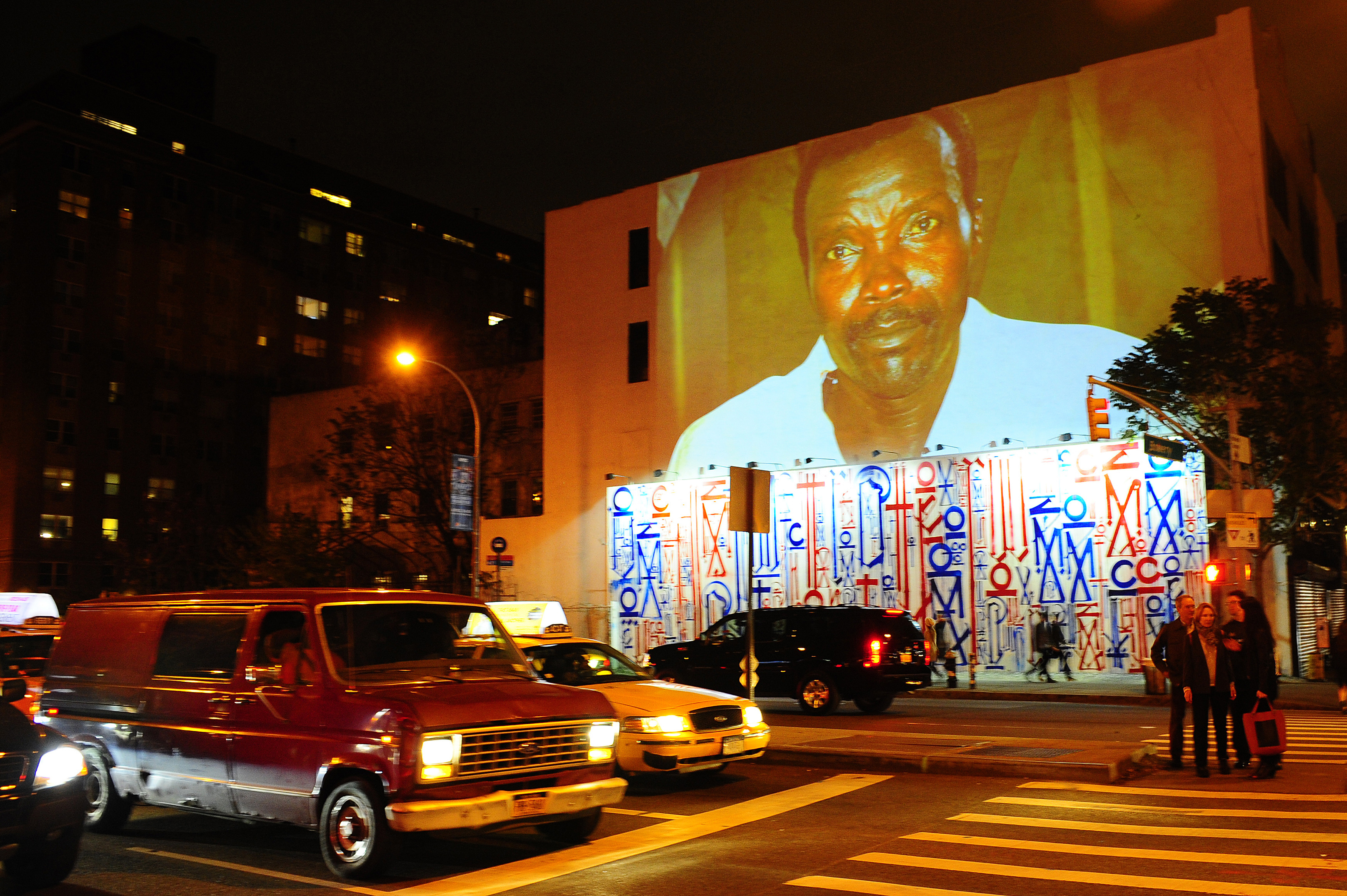 Passersby walk under a projection that is part of the non-profit organization Invisible Children's "Kony 2012" viral video campaign, in New York