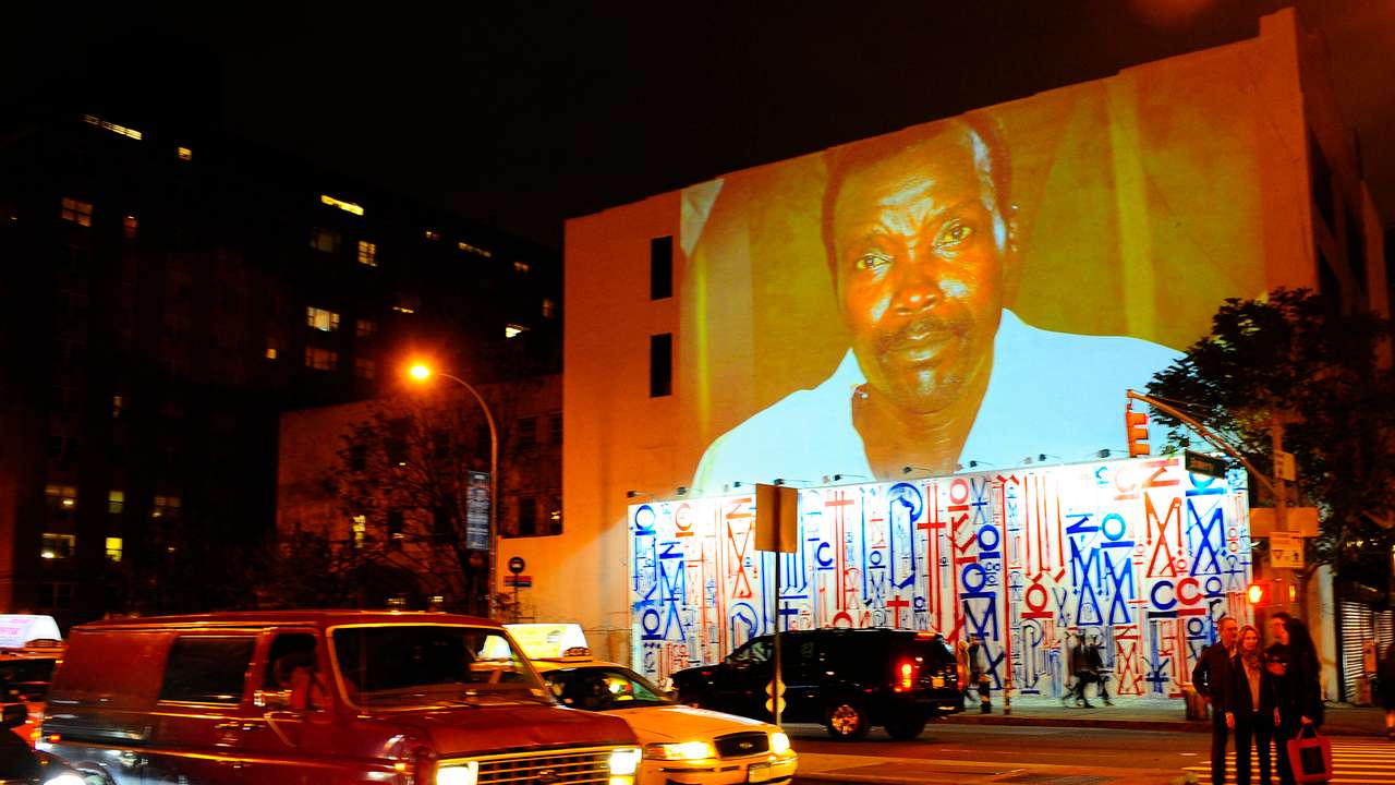 Passersby walk under a projection that is part of the non-profit organization Invisible Children's "Kony 2012" viral video campaign, in New York