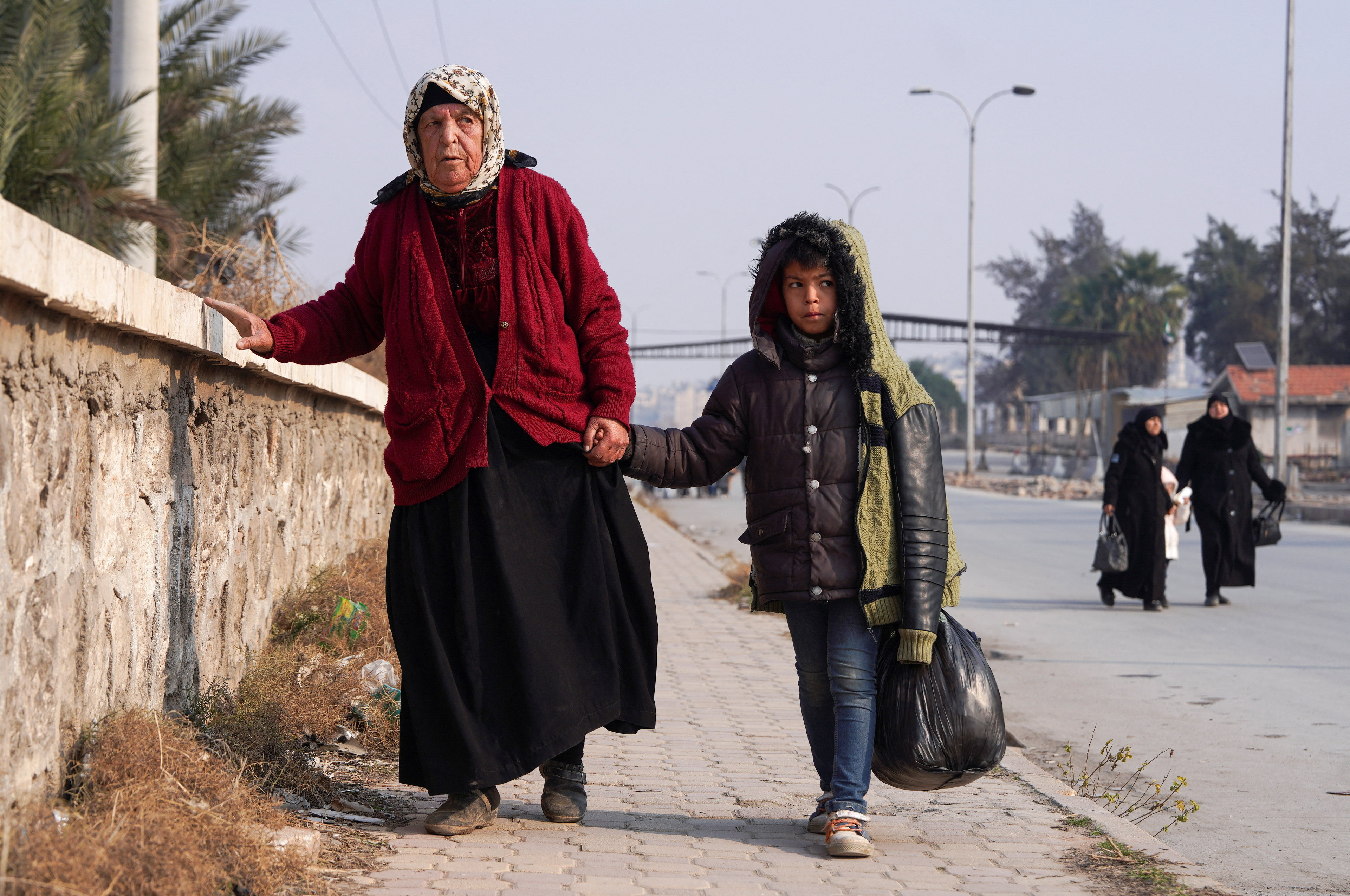 A boy walks with a woman, carrying his belongings, in Aleppo