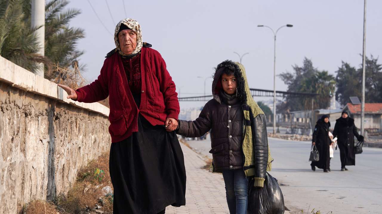 A boy walks with a woman, carrying his belongings, in Aleppo