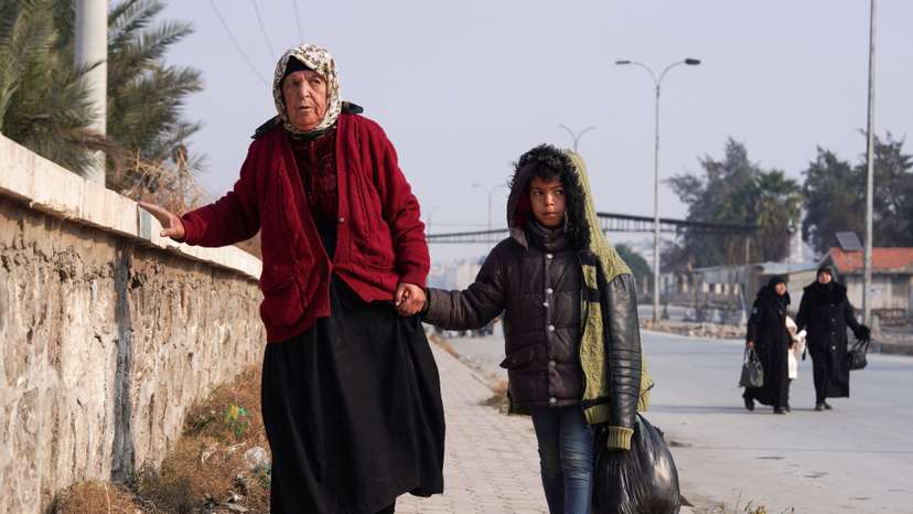 A boy walks with a woman, carrying his belongings, in Aleppo