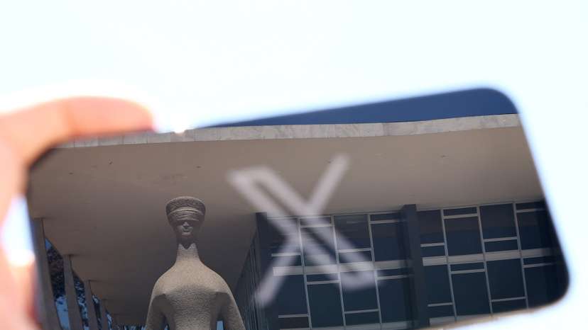 The logo of social media platform X is seen on a mobile phone next to a reflection of Brazil's Supreme Court in this illustration taken August 30, 2024, in Brasilia