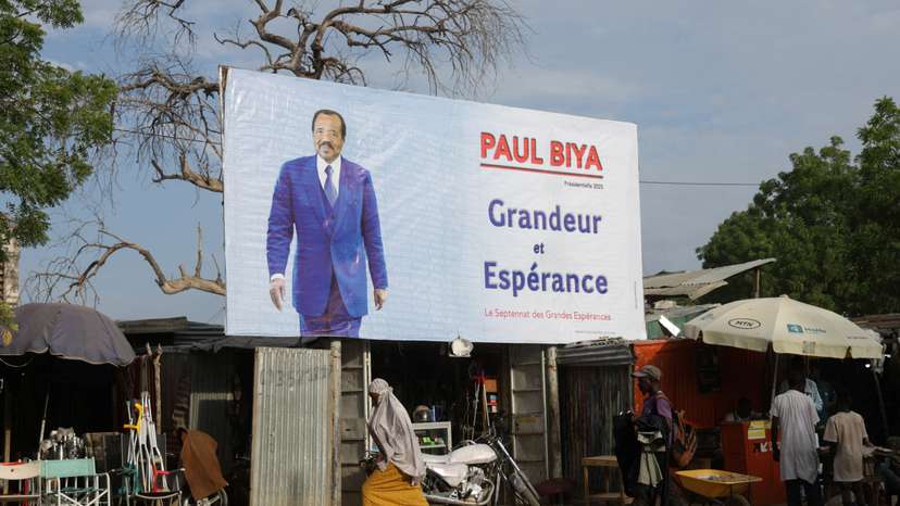 People walk past an election campaign poster for the incumbent President Paul Biya in Maroua, Cameroon