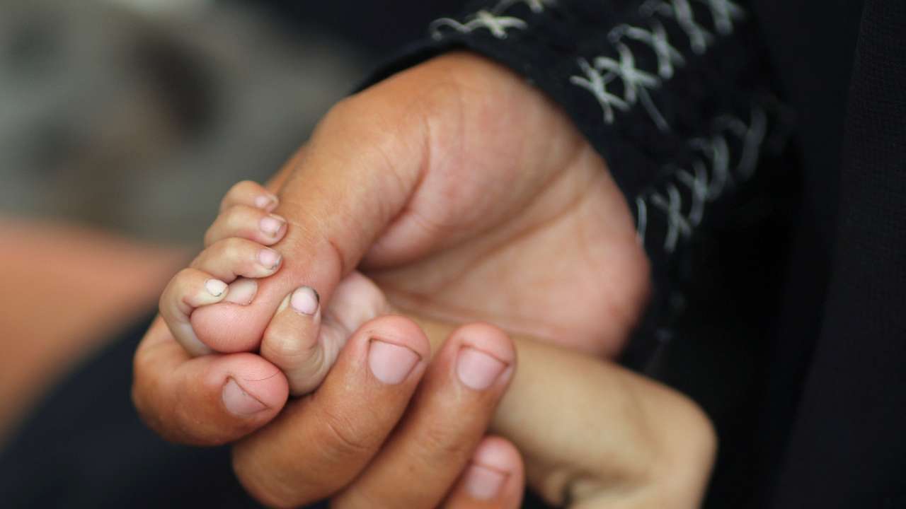 Palestinian mother Amira Muteir holds the hand of her five-month-old baby Ammar, whom she says is wasting away from malnutrition, in Gaza City