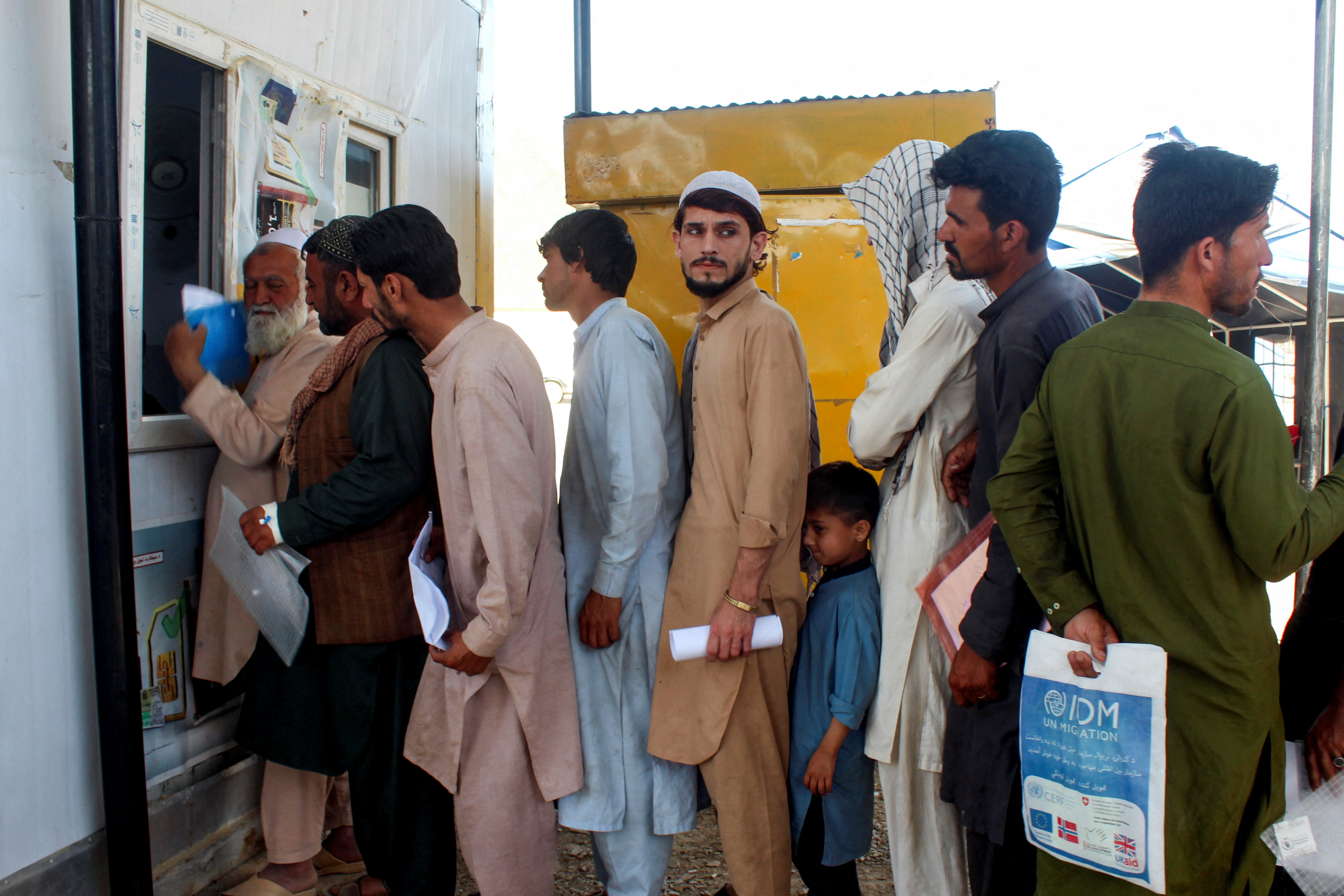 Afghan nationals, who were expelled from Pakistan, stand in queue for registration upon their arrival at the Omari refugee camp in Mohmand Dara