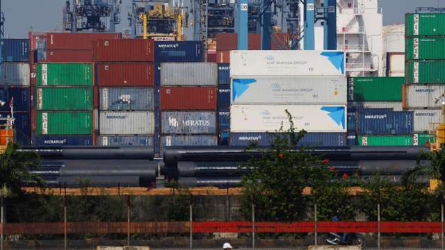 A motorcycle rider drives past stacks of containers at the Tanjung Priok port in Jakarta
