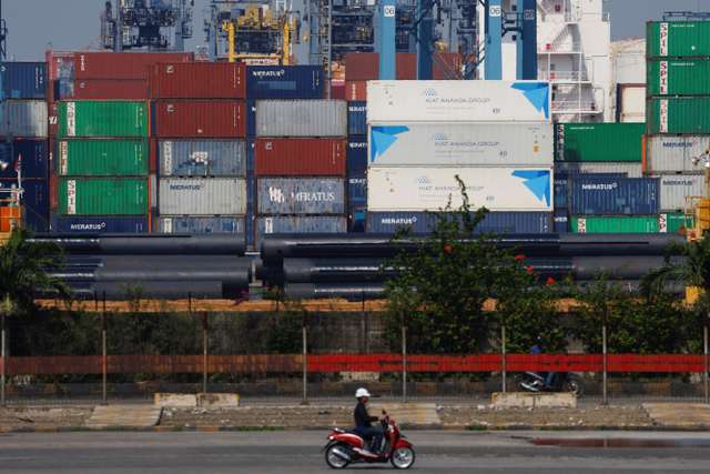 A motorcycle rider drives past stacks of containers at the Tanjung Priok port in Jakarta