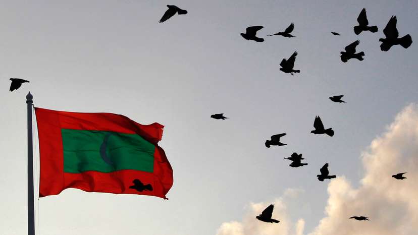 A Maldives national flag flutters as pigeons fly past during the morning in Male