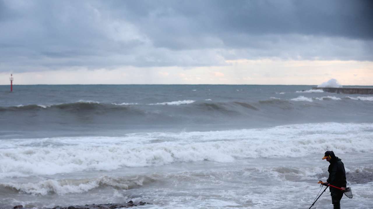 A man looks for metals on La Barceloneta Beach as big waves from a passing storm crash behind him in Barcelona