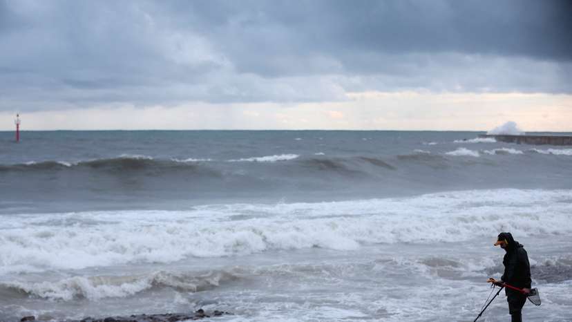 A man looks for metals on La Barceloneta Beach as big waves from a passing storm crash behind him in Barcelona