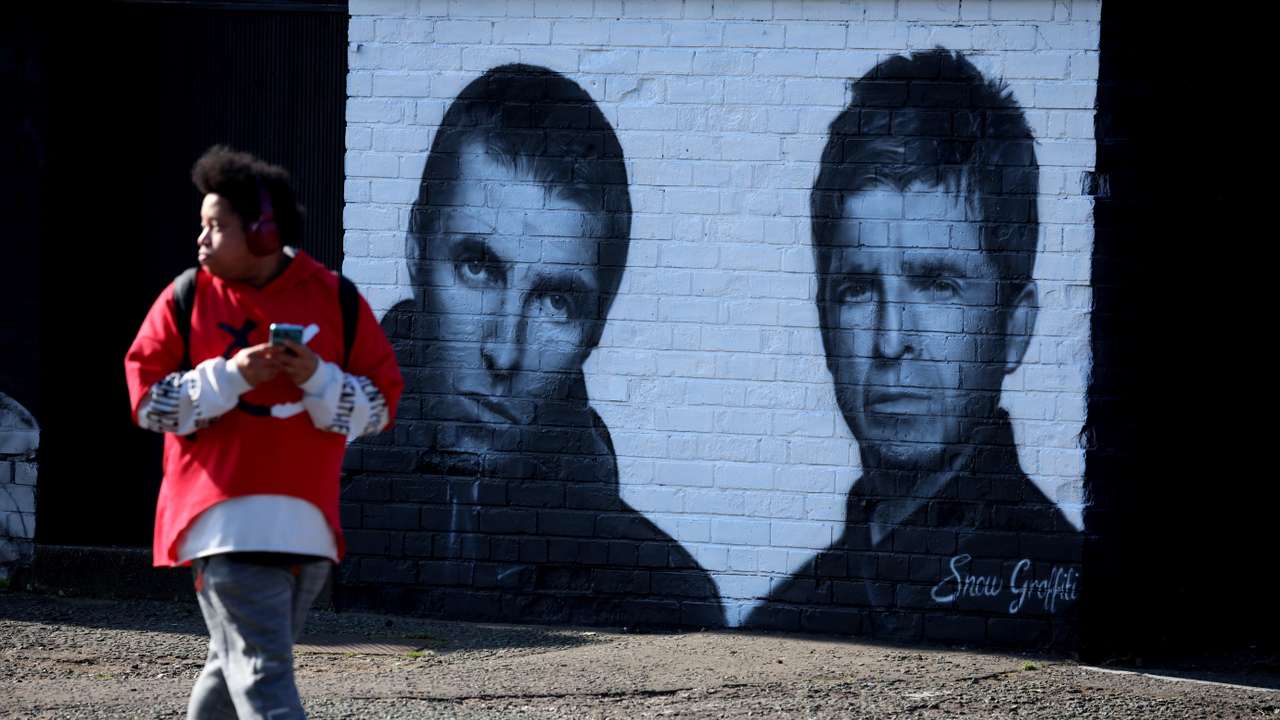 A man walks past a mural of Oasis band members Liam and Noel Gallagher by artist Snow Graffiti on the wall of the Coach and Horses pub in Whitefield, near Manchester