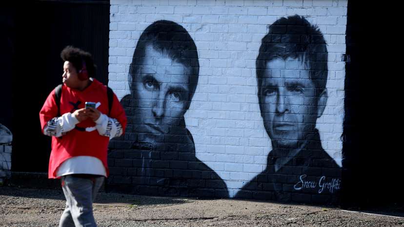 A man walks past a mural of Oasis band members Liam and Noel Gallagher by artist Snow Graffiti on the wall of the Coach and Horses pub in Whitefield, near Manchester