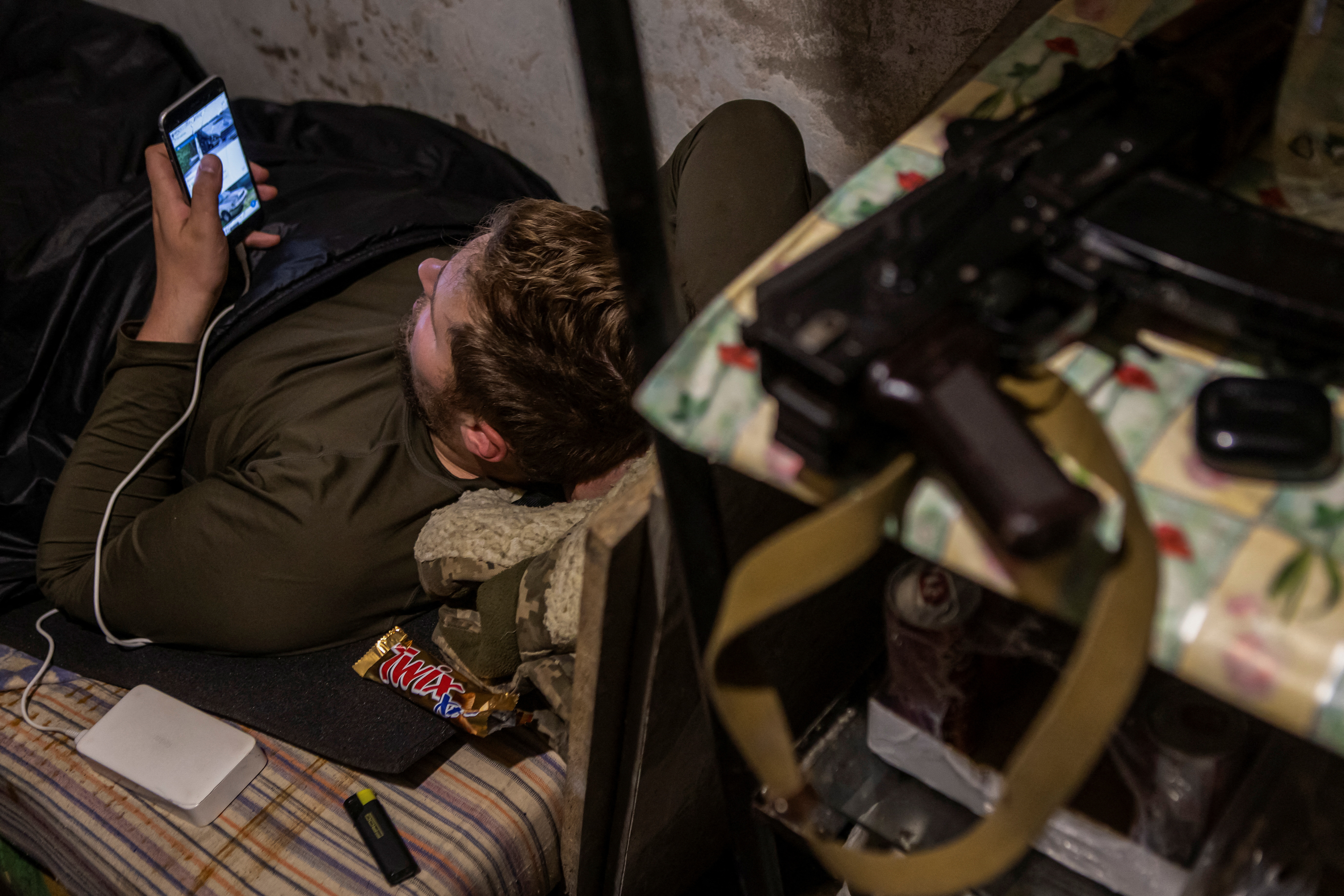 Ukrainian service member uses his smartphone as he rests at a position outside of the frontline town of Bakhmut