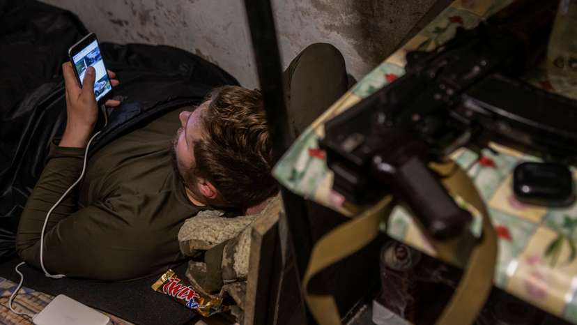 Ukrainian service member uses his smartphone as he rests at a position outside of the frontline town of Bakhmut