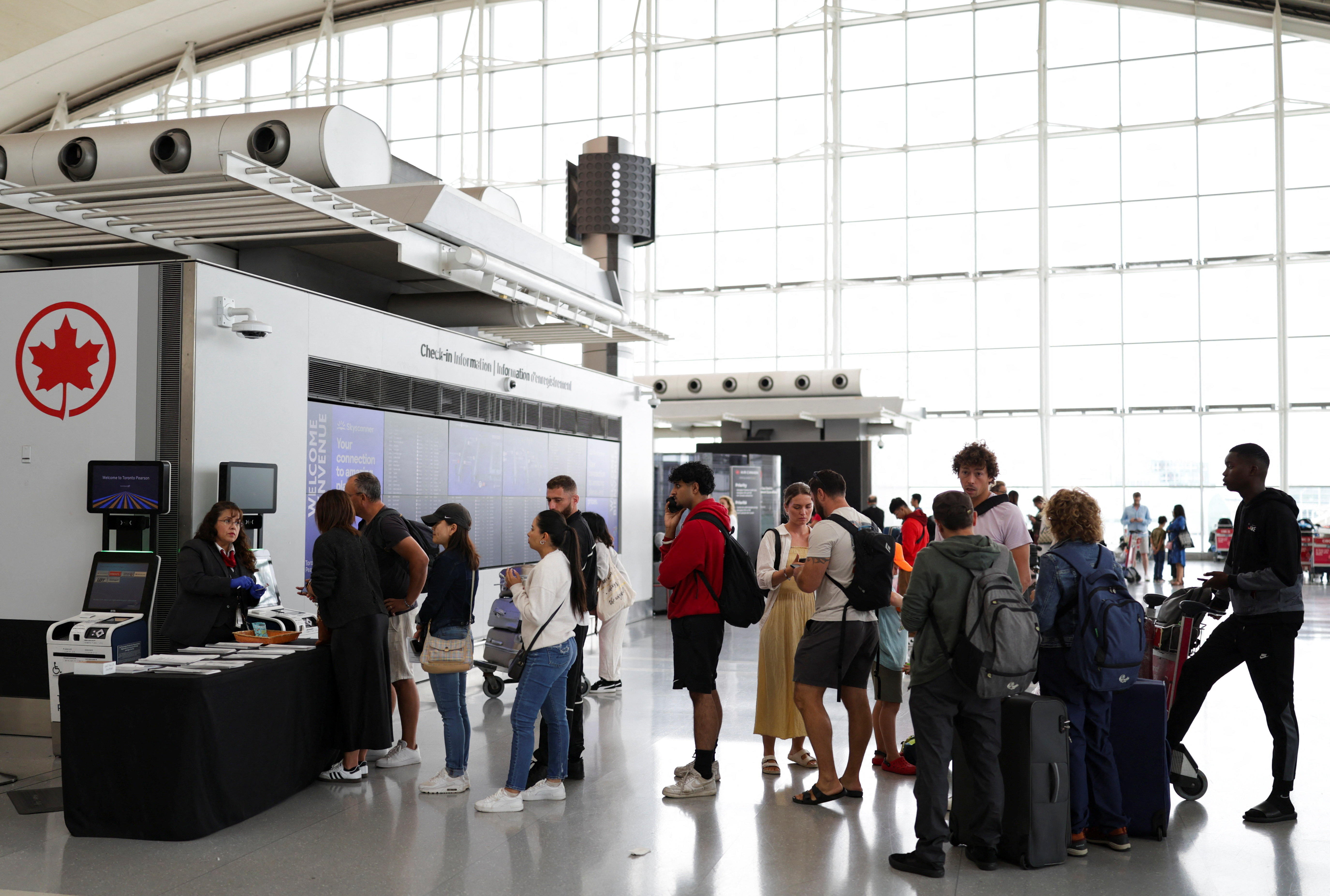 An Air Canada worker stands at a kiosk surrounded by passengers at Toronto Pearson International Airport, following the end of the Air Canada labour strike, in Mississauga