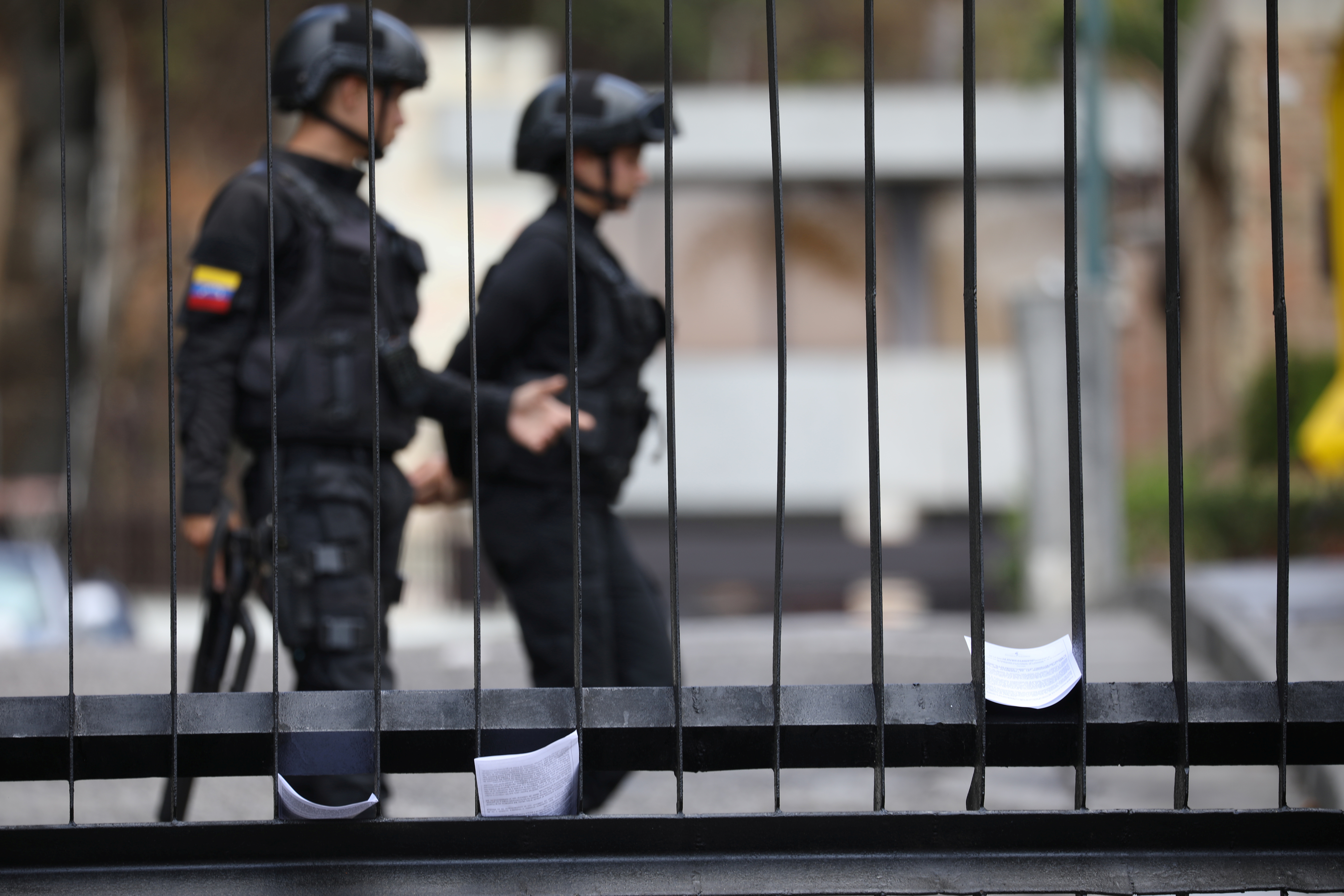 Members of Venezuelan security forces are seen on the background as documents regarding a proposed amnesty law for members of the military, police and civilians stand in a fence of a military facility in Caracas