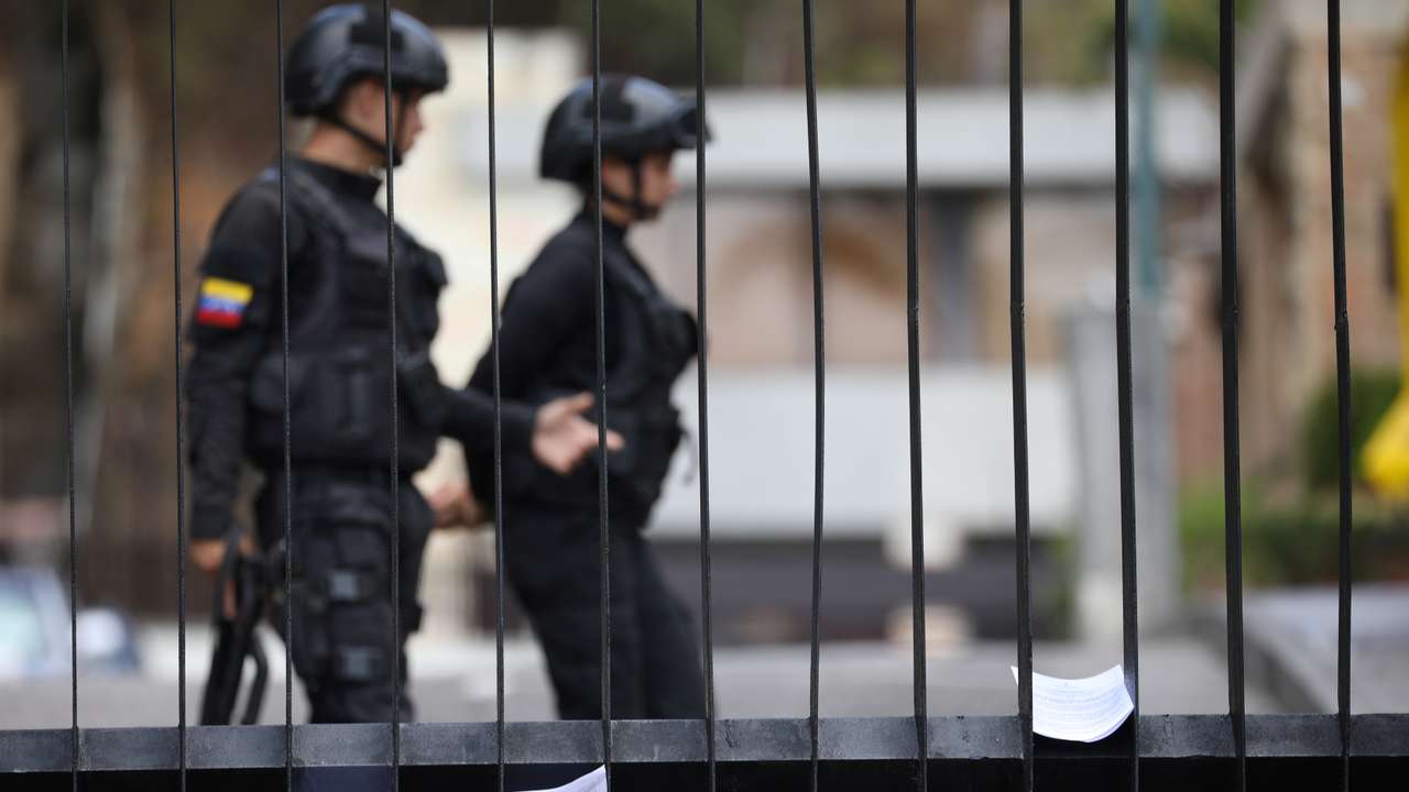 Members of Venezuelan security forces are seen on the background as documents regarding a proposed amnesty law for members of the military, police and civilians stand in a fence of a military facility in Caracas