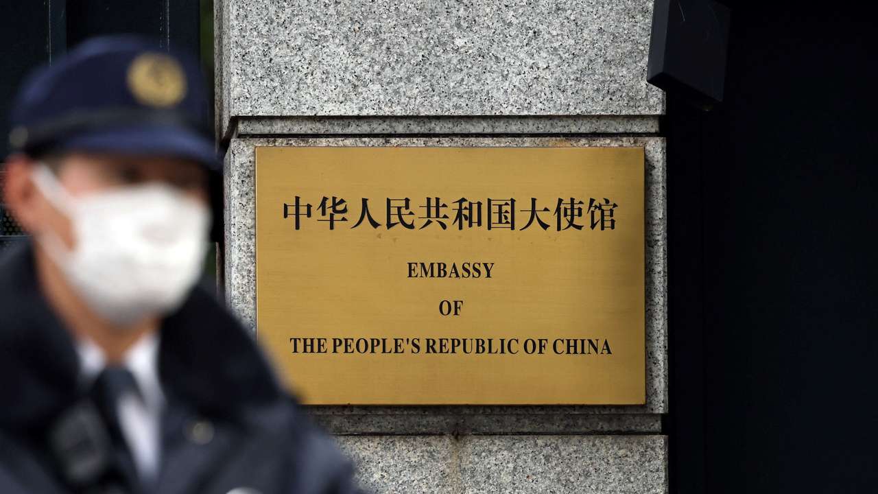 A Japanese police officer stands guard next to a plaque at the entrance of the Chinese embassy in Tokyo