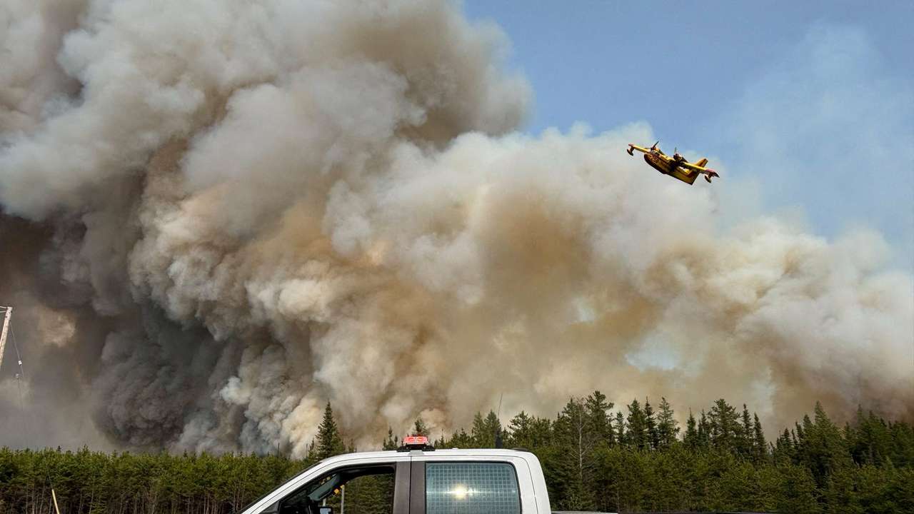 Water bomber flies over the plume of smoke from a wildfire near The Pas