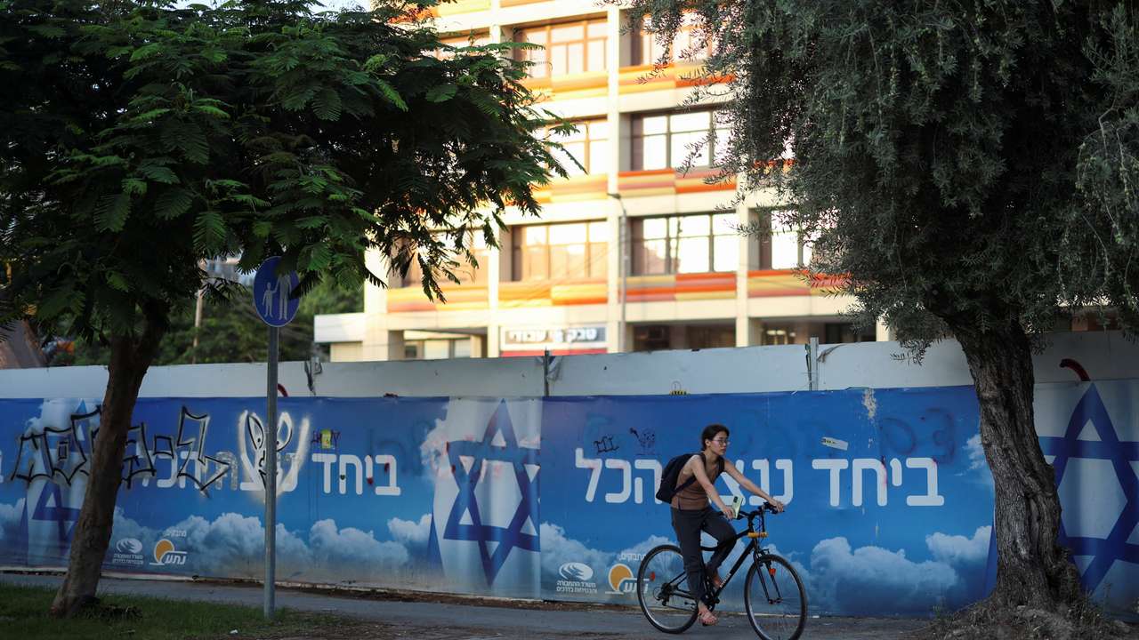 A woman on a bicycle rides past a billboard with the Israeli flag and a slogan in support of the hostages kidnapped during the deadly October 7 attack displayed, in Tel Aviv