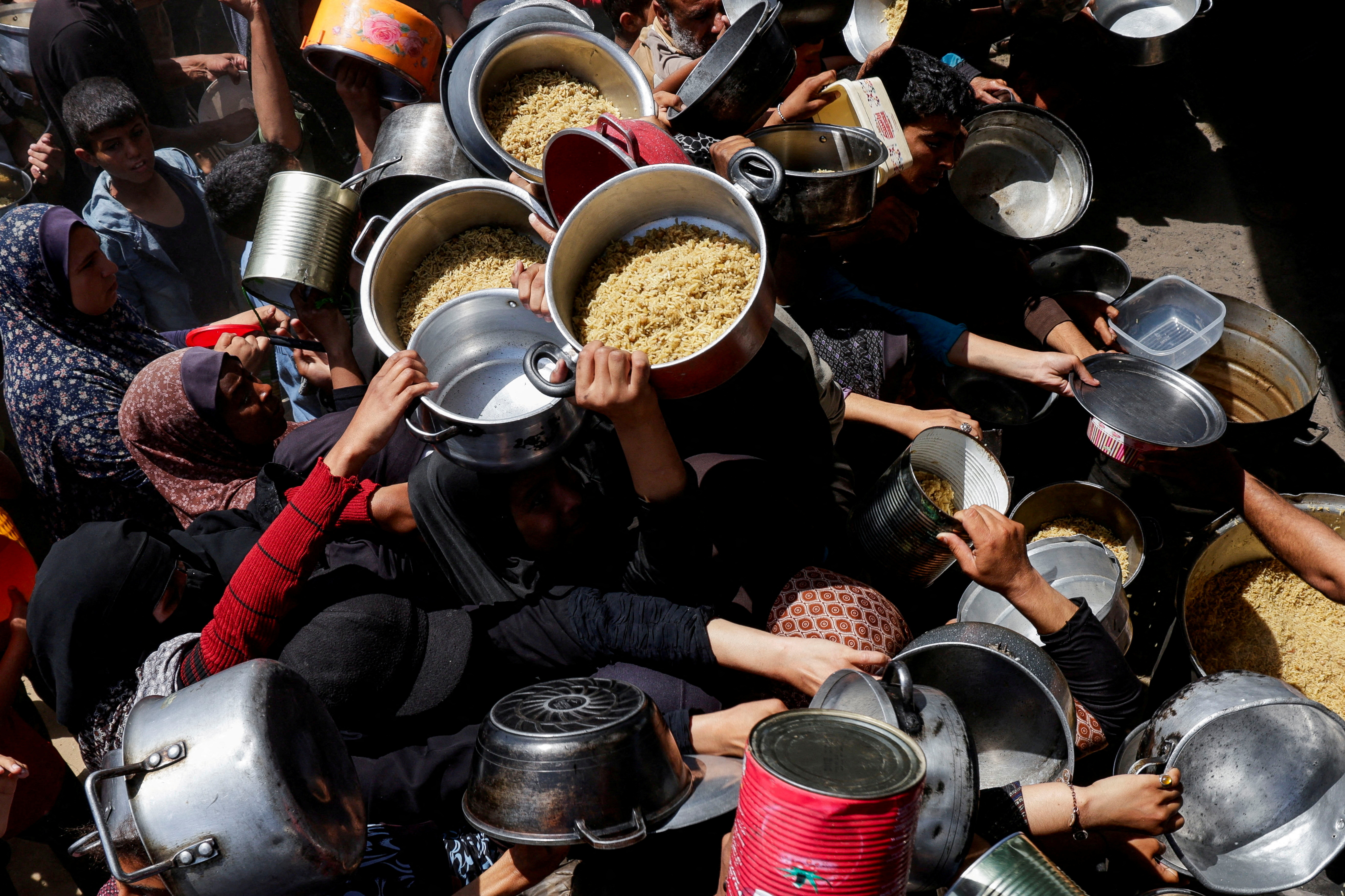 Palestinians wait to receive food cooked by a charity kitchen, in Khan Younis