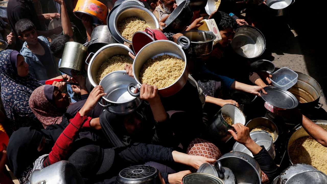 Palestinians wait to receive food cooked by a charity kitchen, in Khan Younis