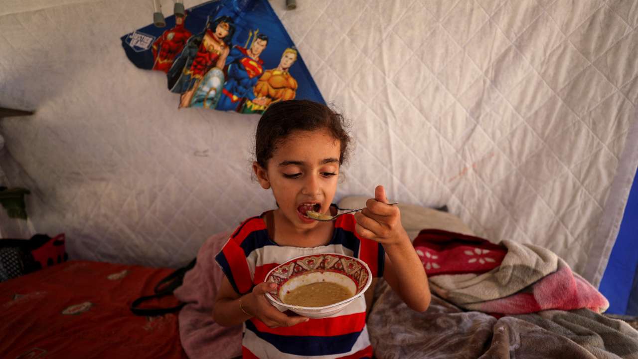 Eyala, the daughter of displaced Palestinian man Nizar Bakron, eats inside their tent, in Gaza City