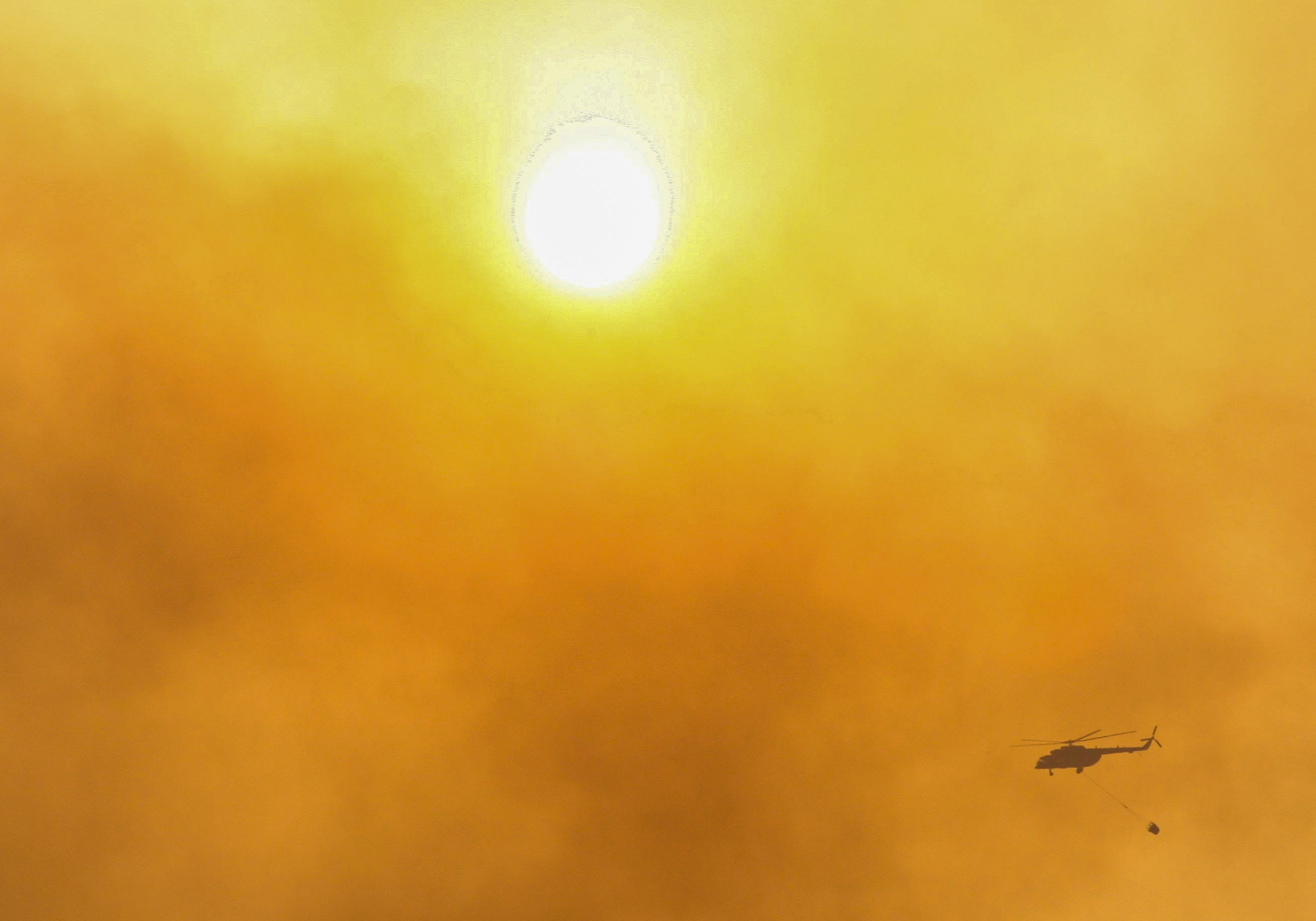 A firefighting helicopter flies through the smoke near Marmaris