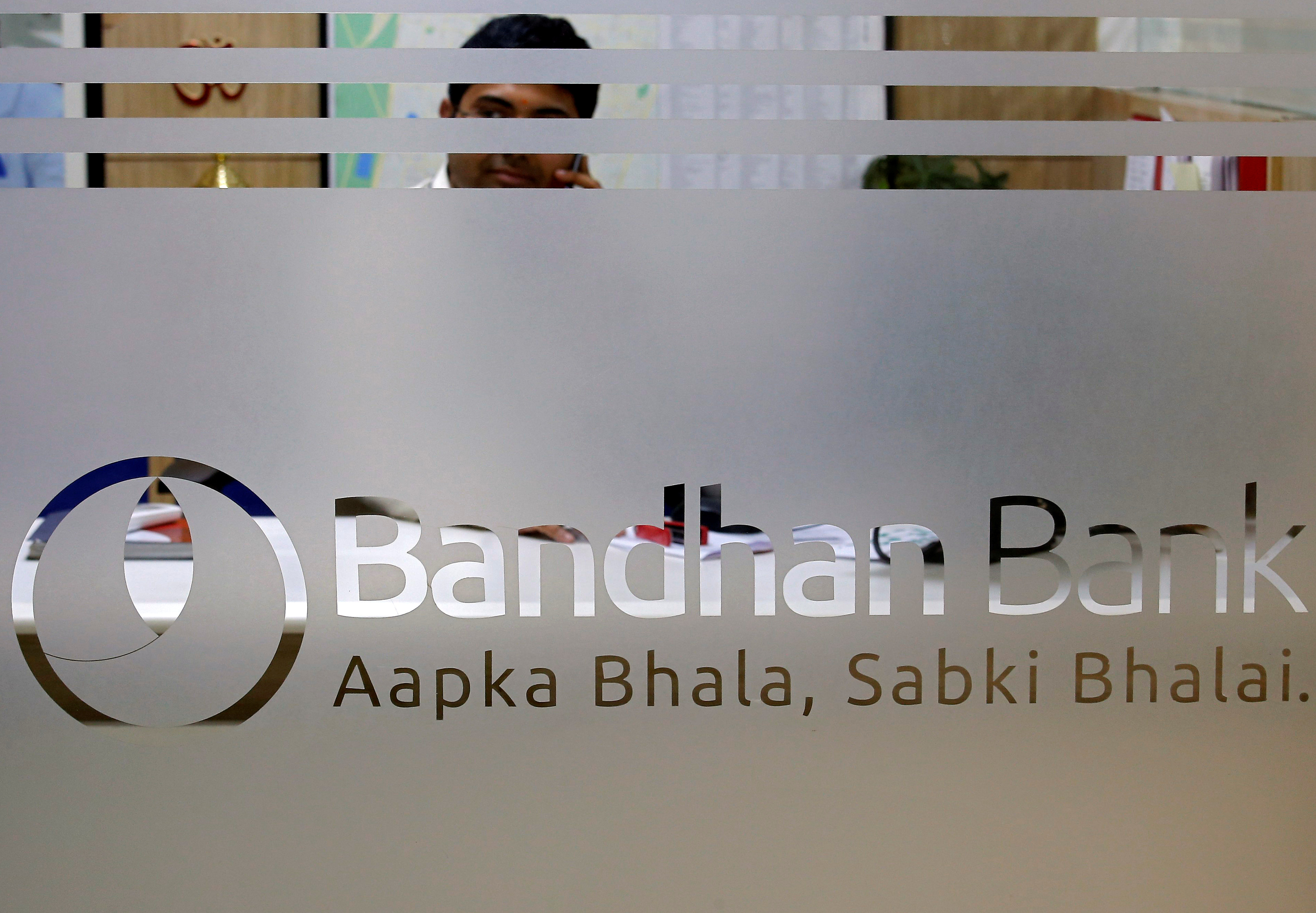 An employee of Bandhan Bank is seen behind a glass bearing the bank's logo inside a branch office in Kolkata