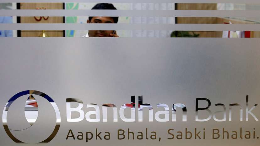 An employee of Bandhan Bank is seen behind a glass bearing the bank's logo inside a branch office in Kolkata