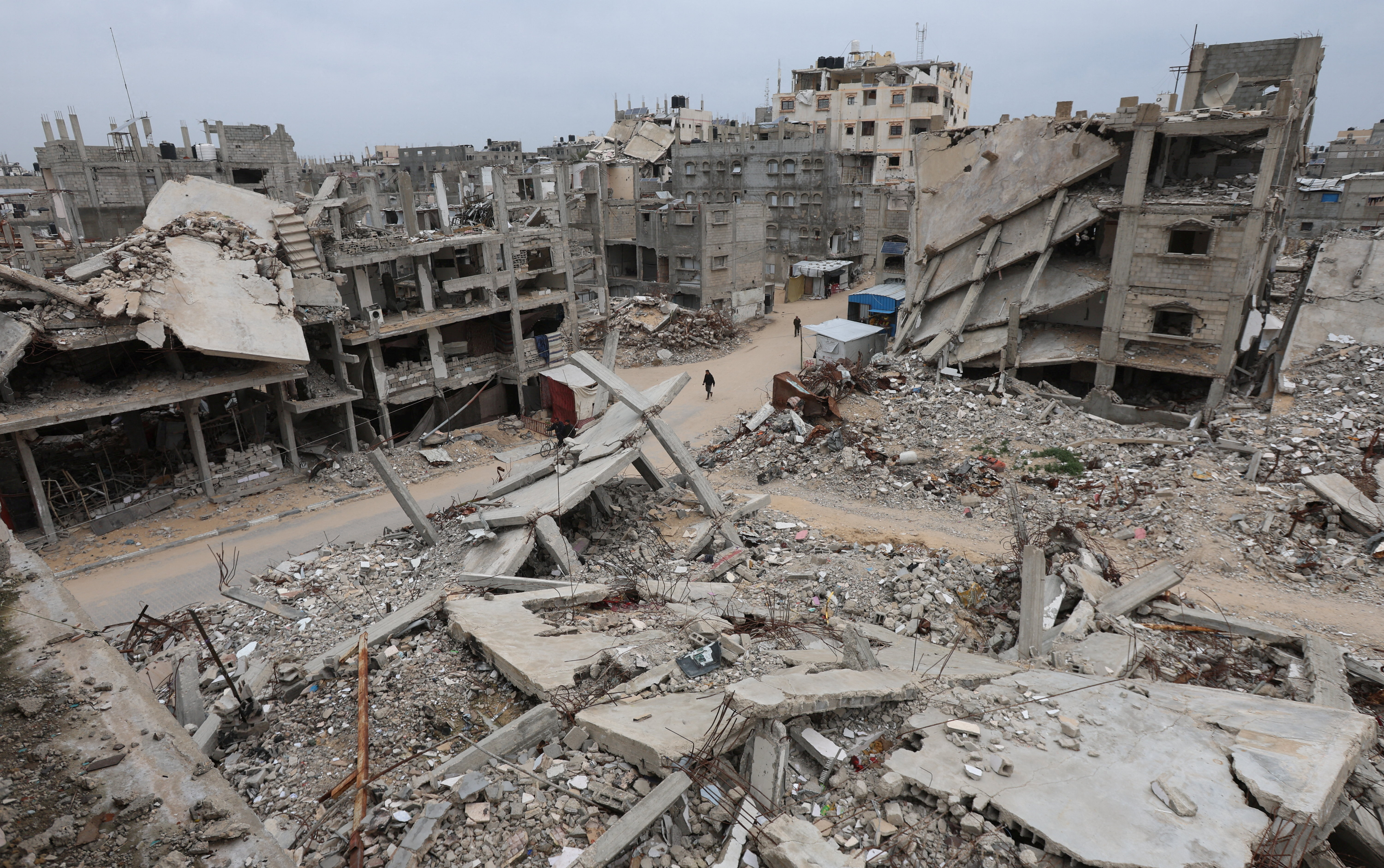 Palestinians walk surrounded by the rubble of houses destroyed in Israeli strikes during the war, in Khan Younis