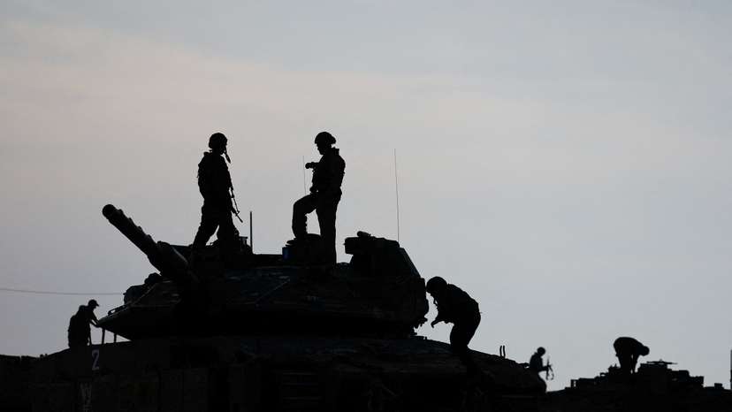 Israeli soldiers are silhouetted as they stand on a tank, near the Israel-Gaza border
