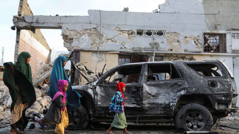 Somalis walk past the wreckage of a vehicle at the scene of an explosion outside a restaurant where patrons were watching the final of the Euro 2024 football tournament on TV, in Bondhere district of Mogadishu