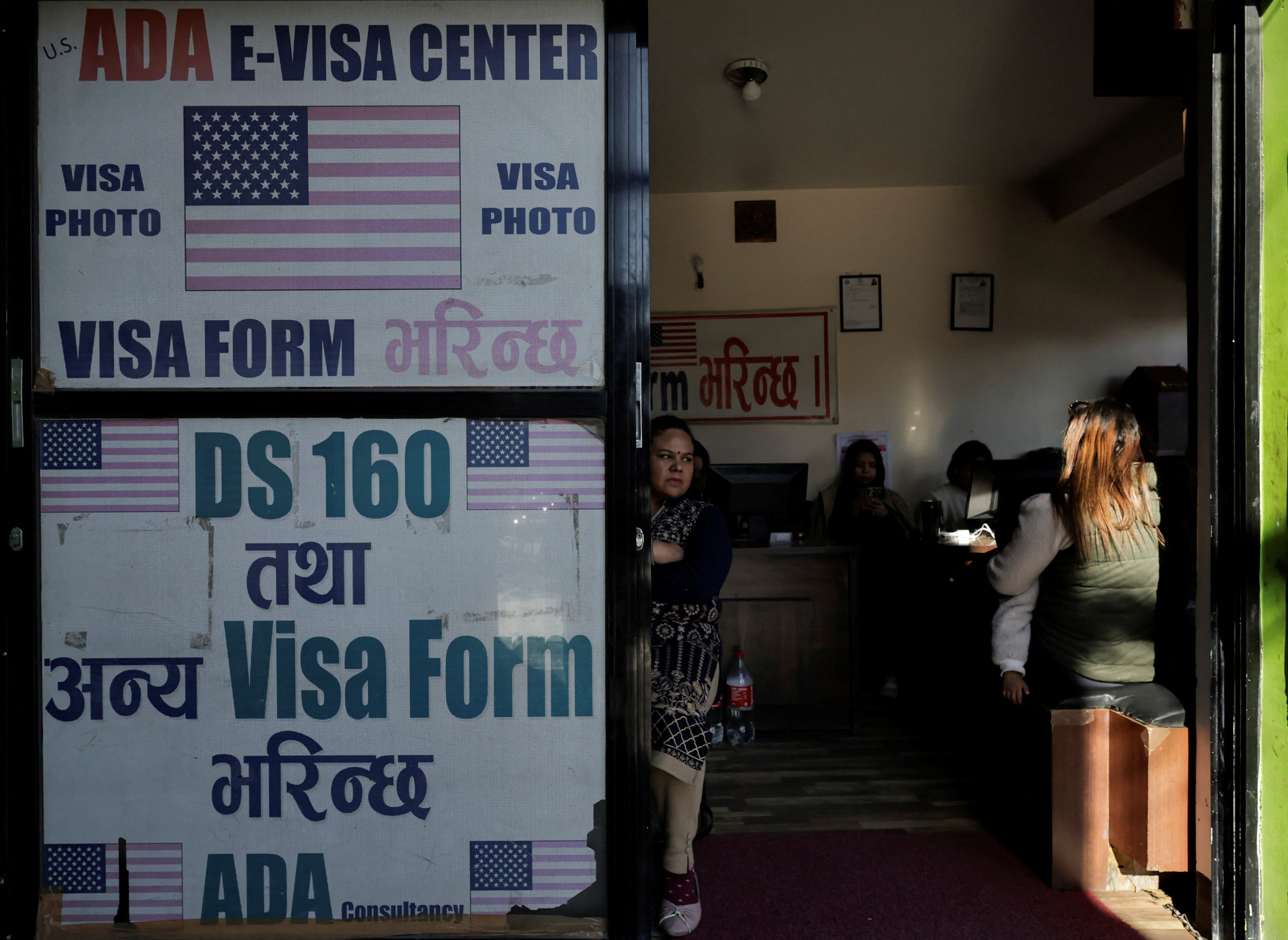 A woman holding a child sits at a visa consultancy, in Kathmandu