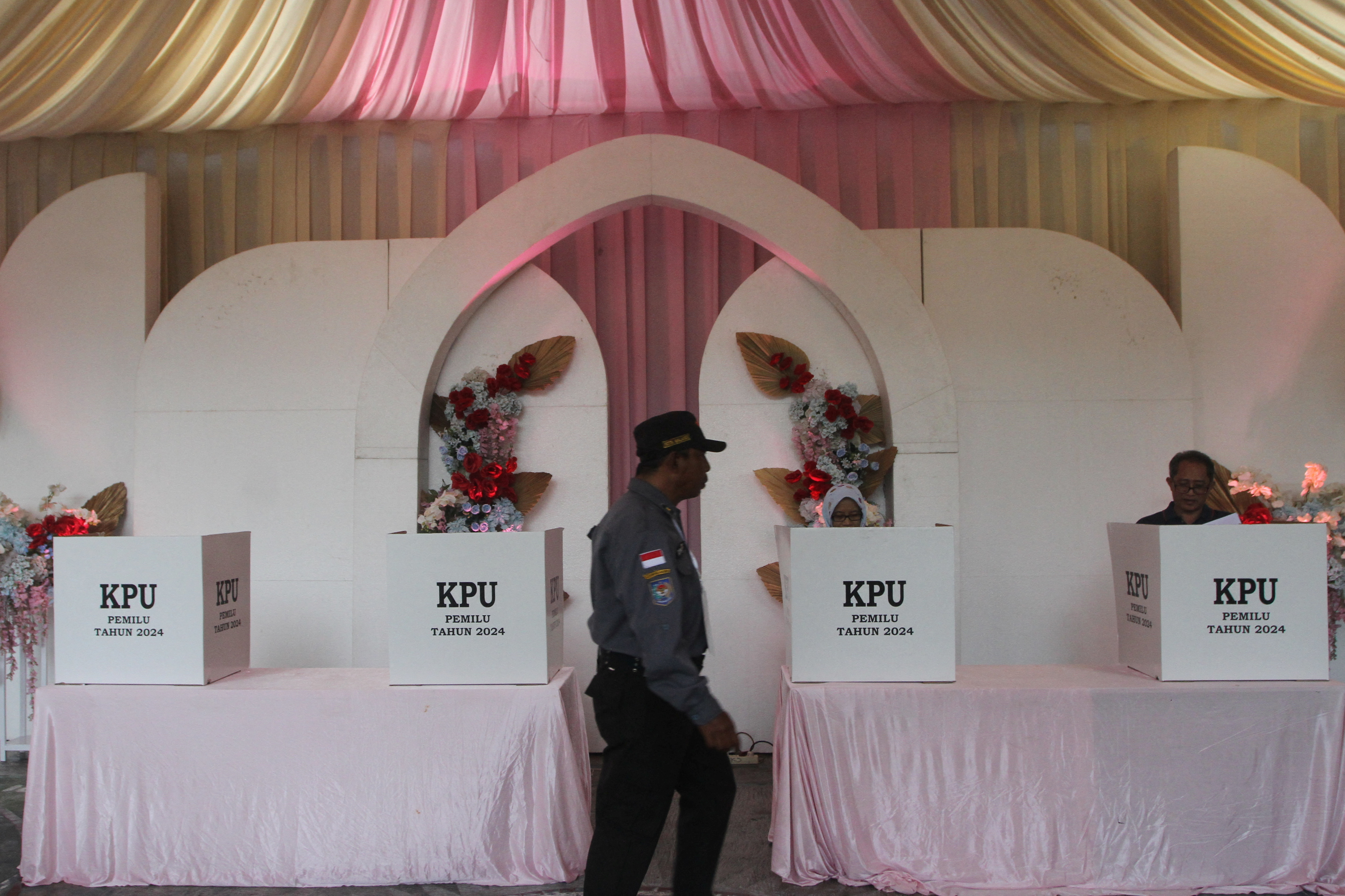 A member of the Linmas civil defence force passes by ballot boxes at a Valentine’s Day themed polling station during the general election in Malang