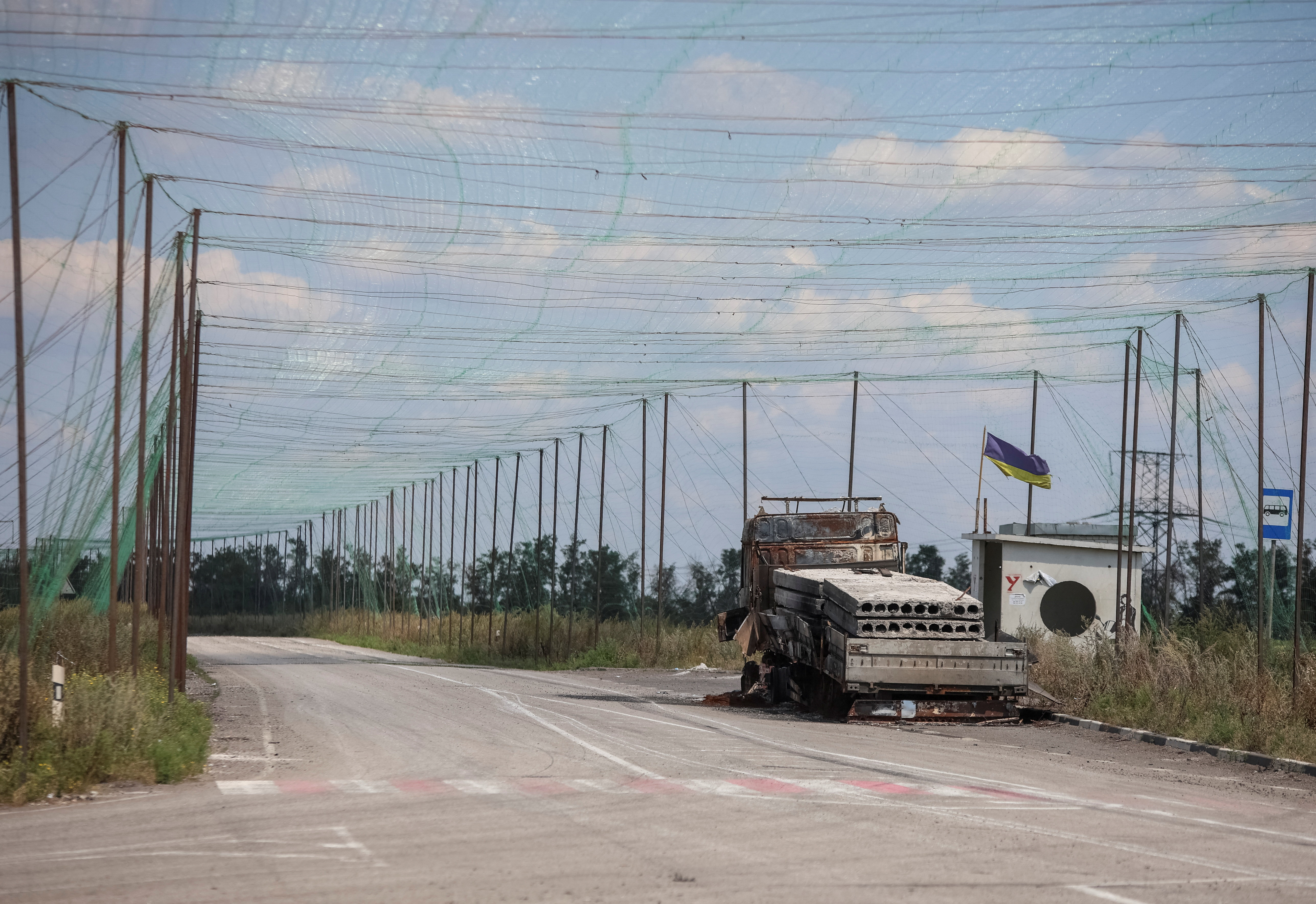 A view shows a burned vehicle and anti-drone nets installed over a road near the frontline town of Dobropillia