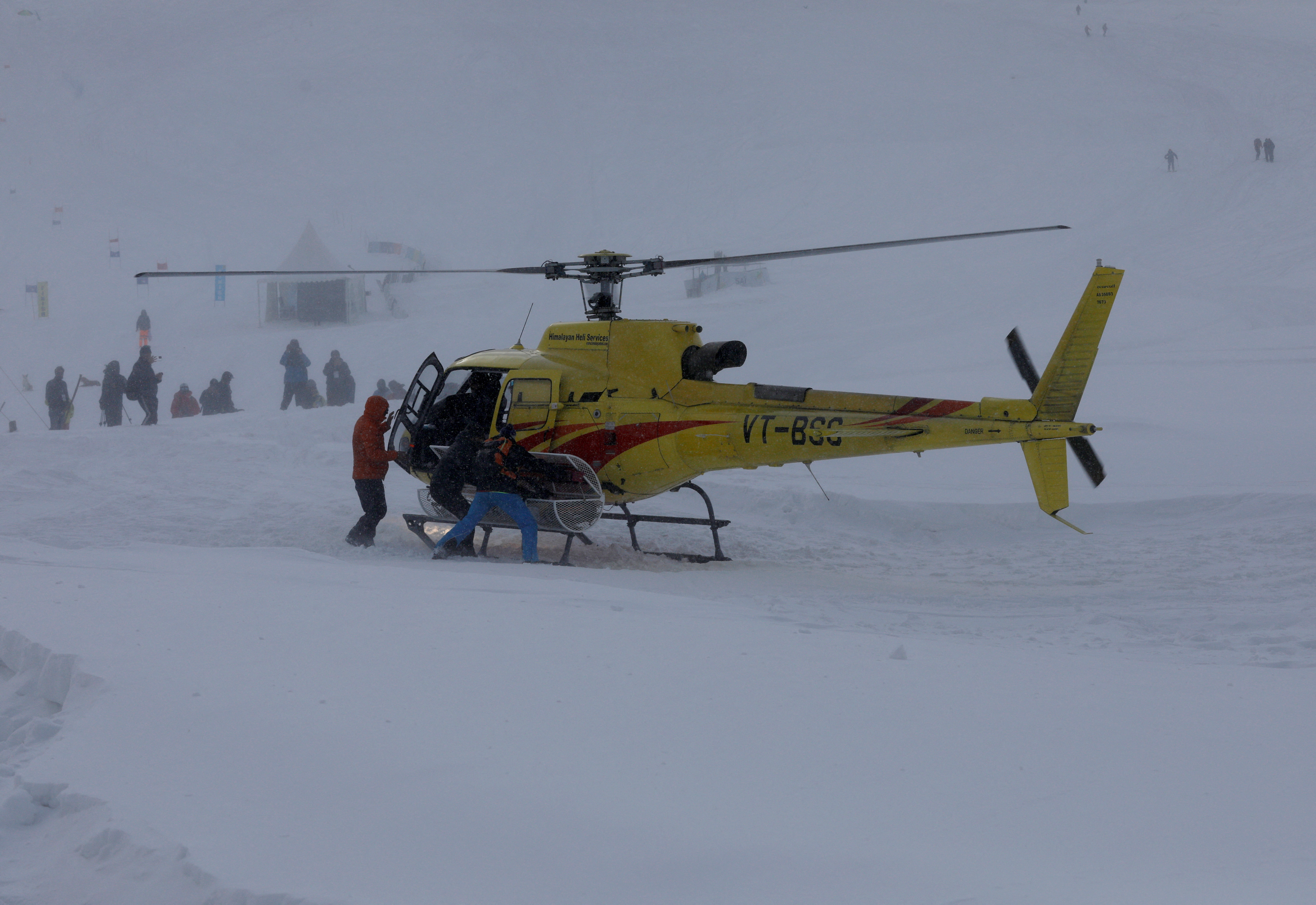 Members of a rescue team pick up a trolley from a helicopter to airlift the body of a foreign skier, in Kongdoori