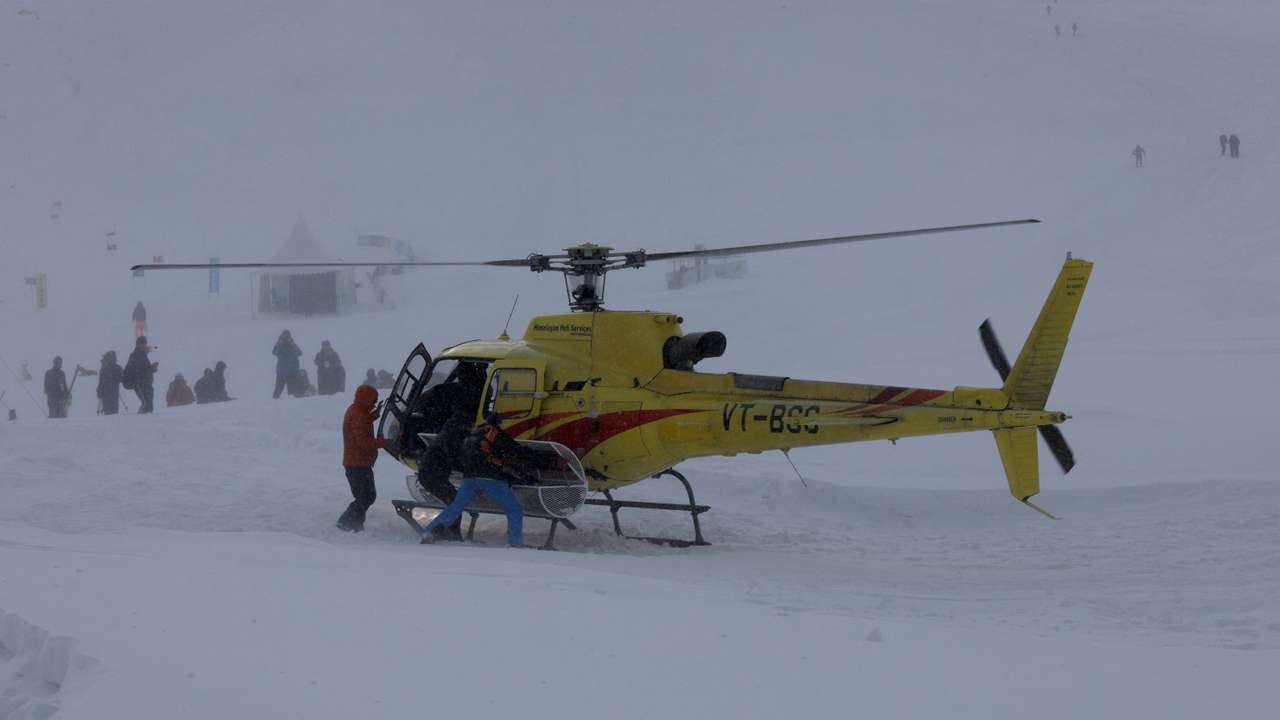 Members of a rescue team pick up a trolley from a helicopter to airlift the body of a foreign skier, in Kongdoori