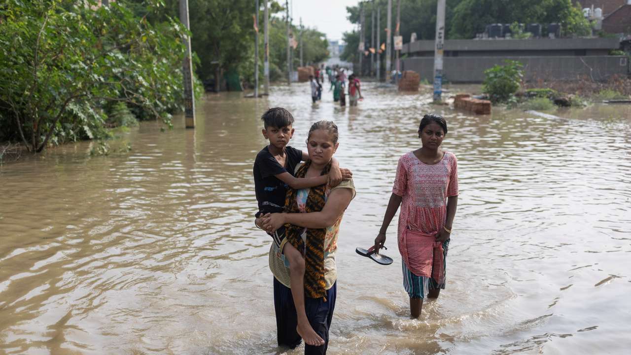 A woman carries her son as she walks through a flooded road after a breach in a canal that supplies water from a nearby state, in New Delhi