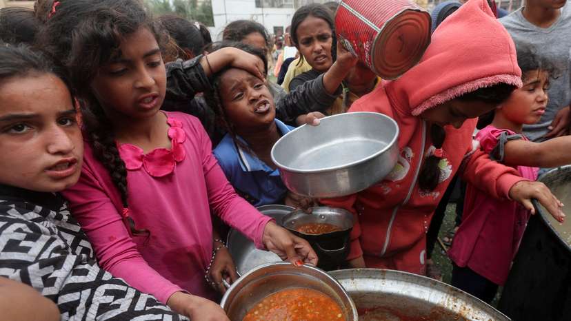Palestinians wait to receive food cooked by a charity kitchen, in Nuseirat