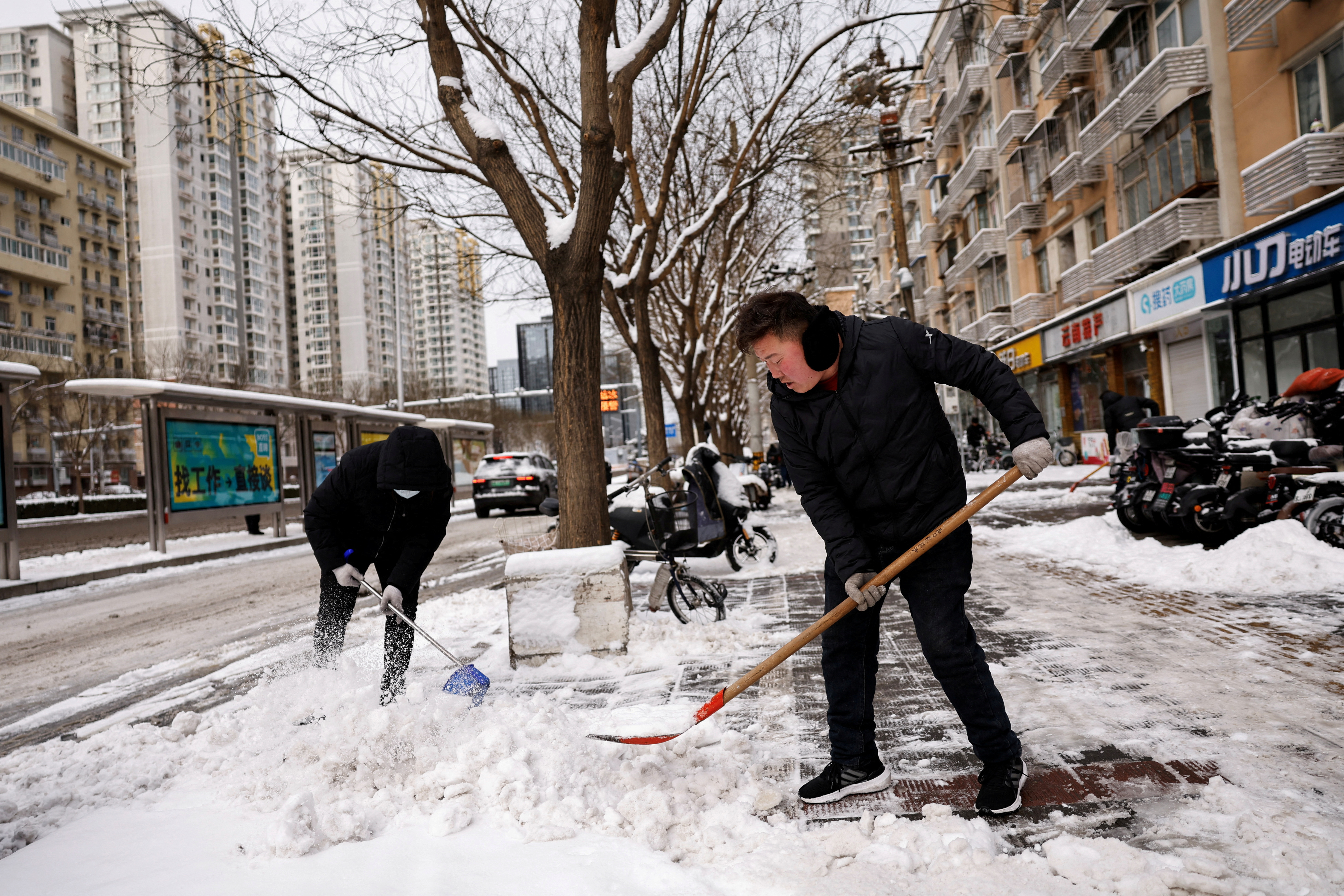 Workers clear snow off a pedestrian road following snowfall in Beijing