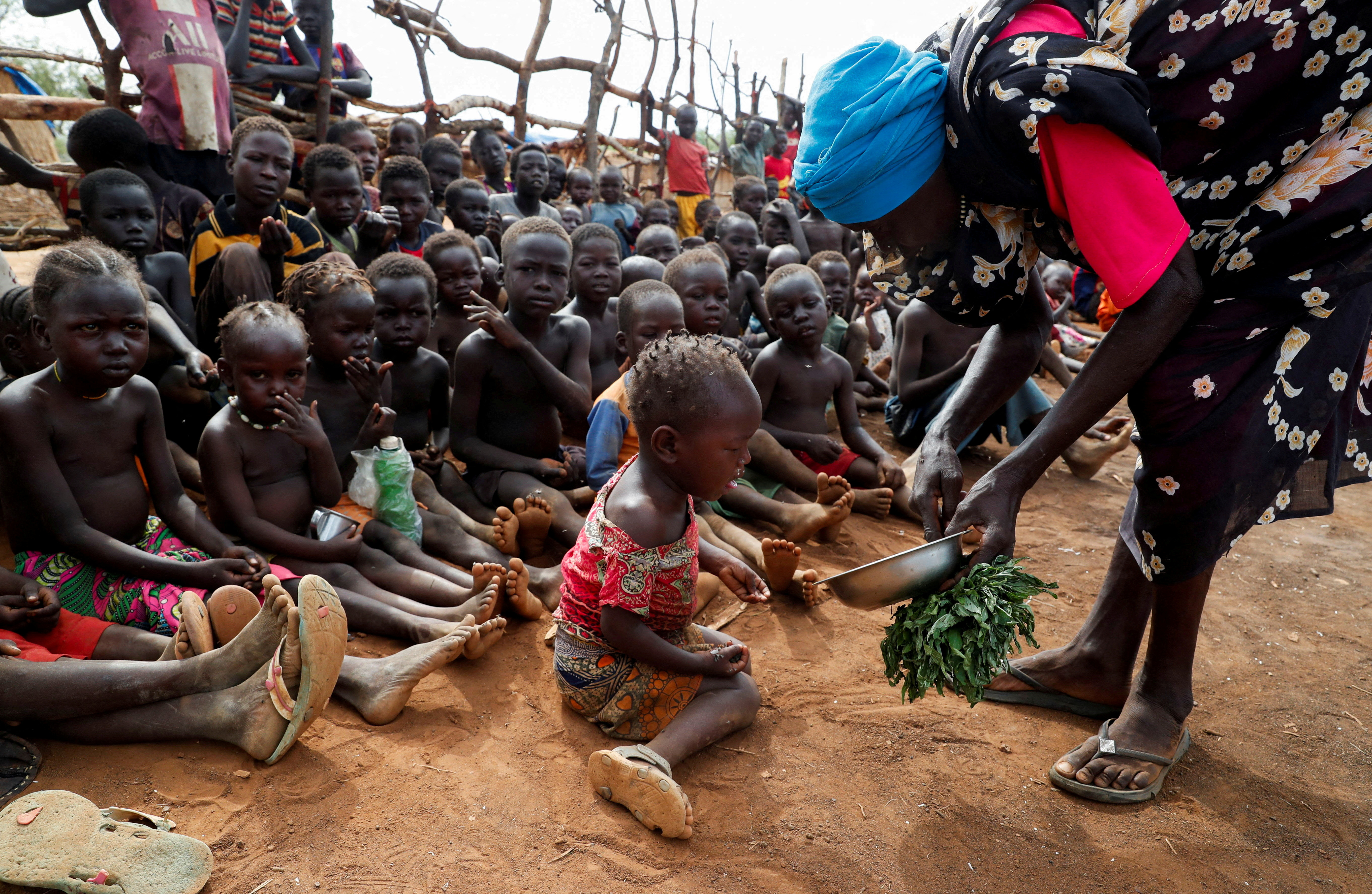 FILE PHOTO: Asha Kano Kavi, an internally displaced woman from Kadugli, serves wild boiled leaves for food to orphaned children at the Bruam IDP Camp in the Nuba Mountains, South Kordofan, Sudan