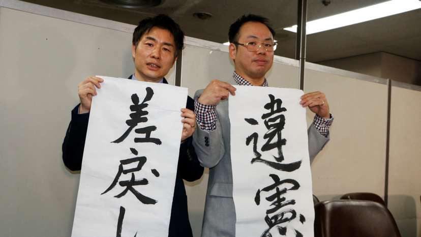 The Plaintiff's lawyers, Kazuyuki Minami and Masafumi Yoshida, hold banners that read "returned" and "unconstitutional", in Tokyo