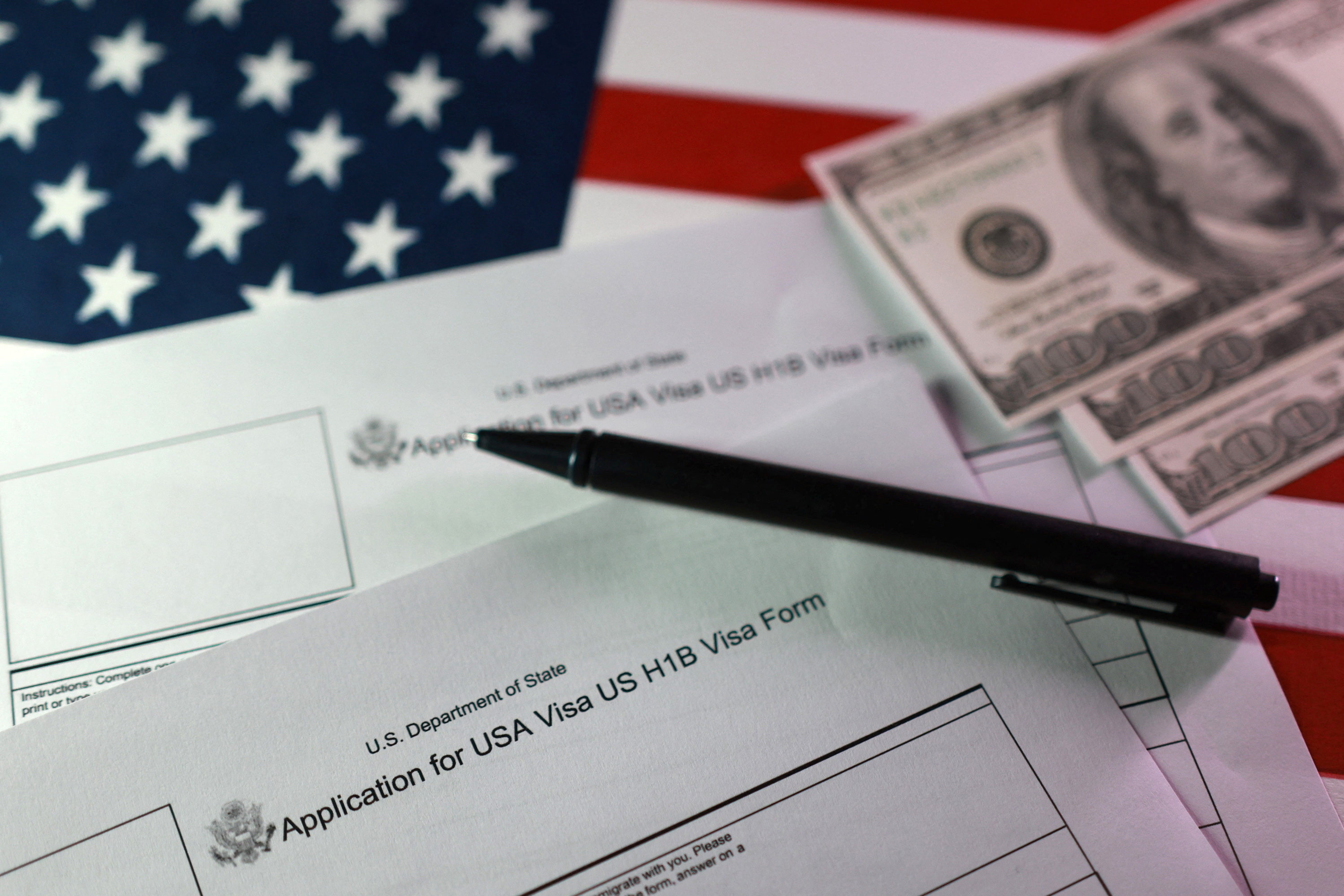 Illustration shows U.S. flag, mock U.S. dollars and U.S. H-1B Visa application forms