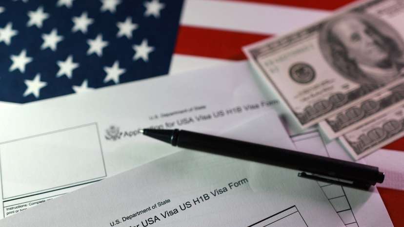 Illustration shows U.S. flag, mock U.S. dollars and U.S. H-1B Visa application forms