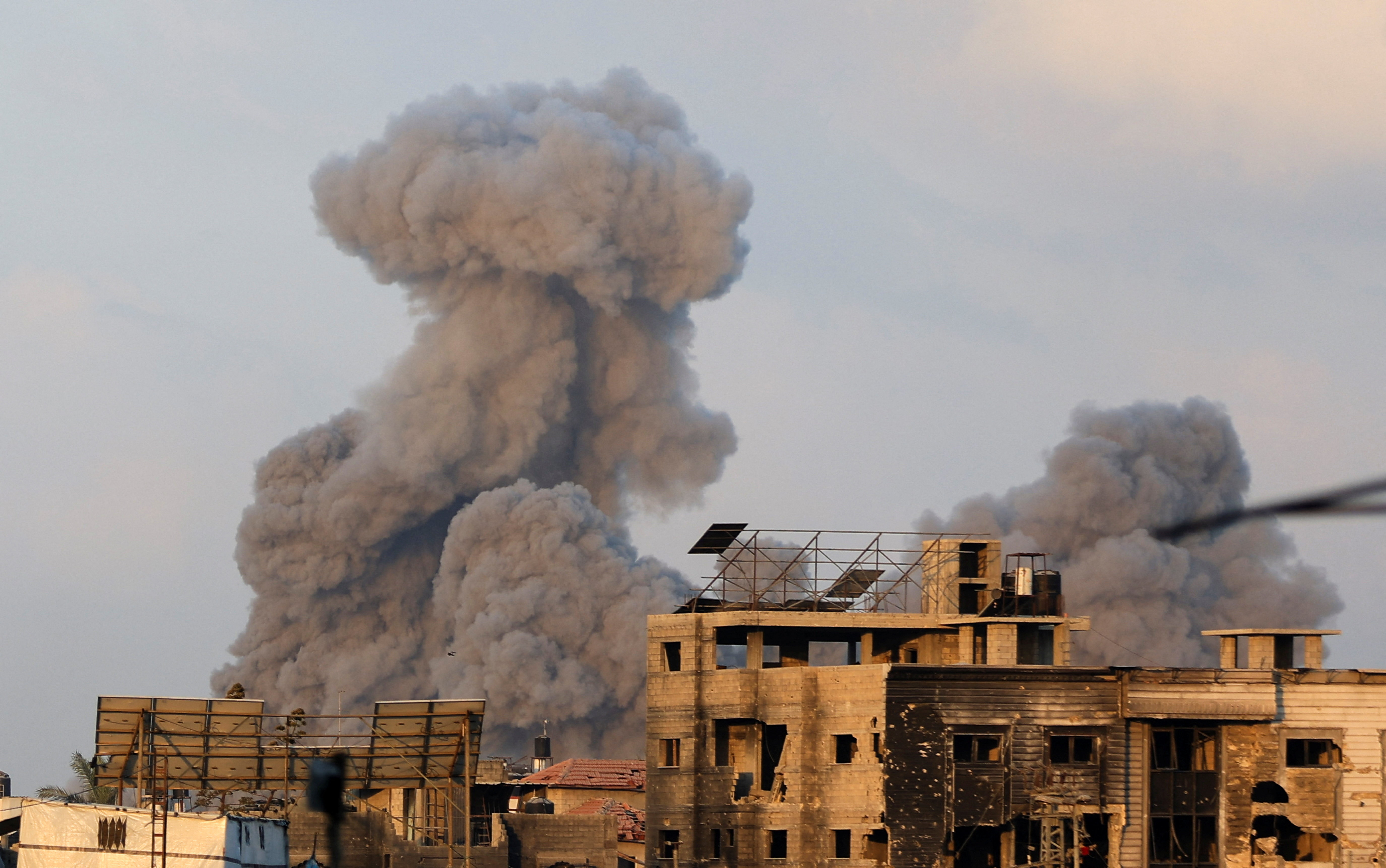 Palestinians stand as smoke rises following an Israeli strike, in Gaza City