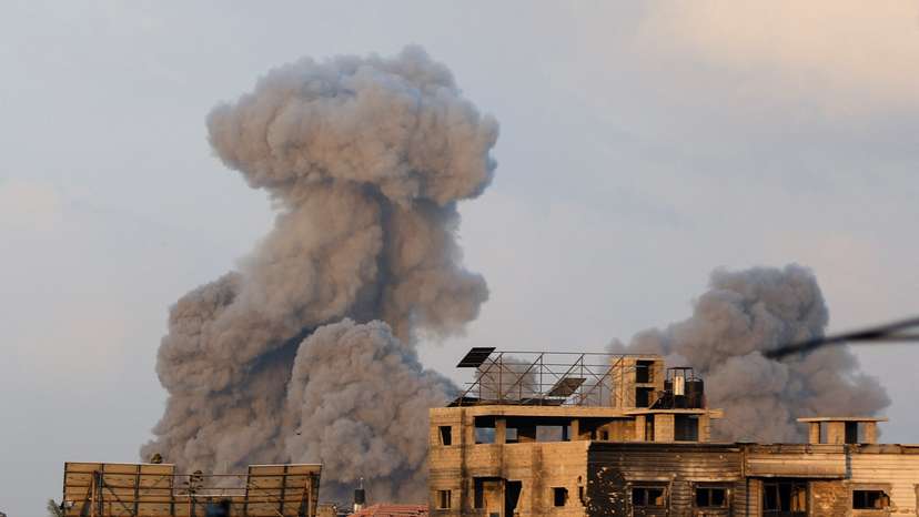 Palestinians stand as smoke rises following an Israeli strike, in Gaza City