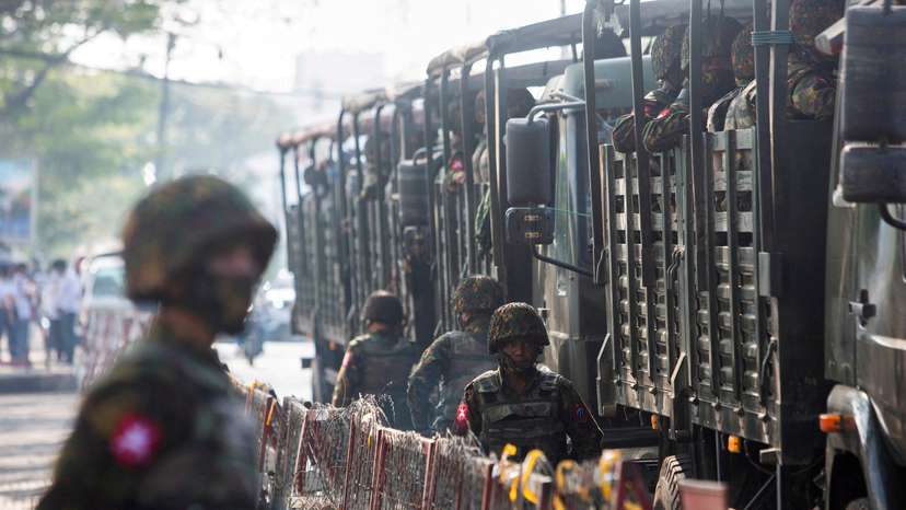 FILE PHOTO: Soldiers stand next to military vehicles as people gather to protest against the military coup, in Yangon
