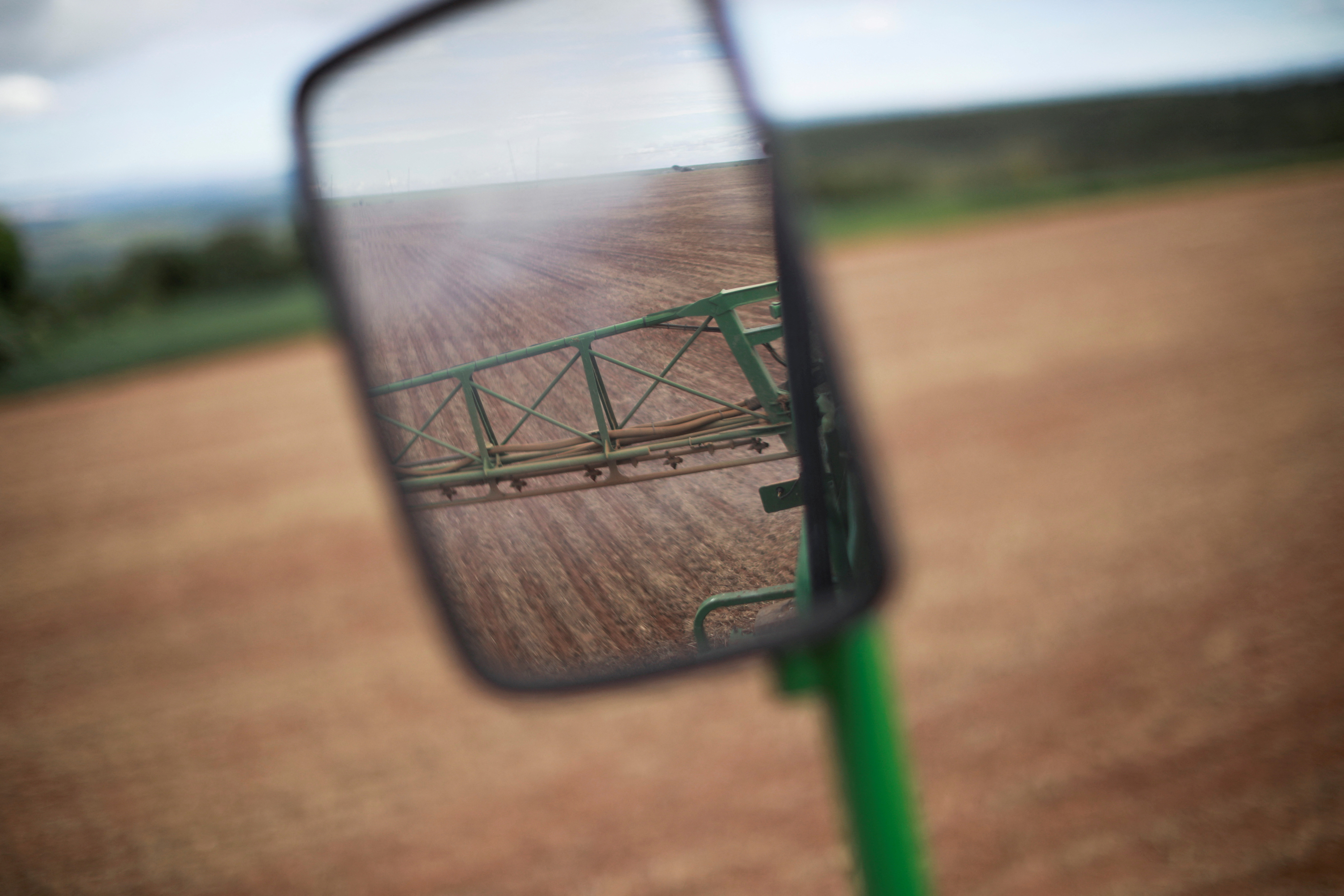 FILE PHOTO: A side-view mirror of a tractor shows herbicide being sprayed in a field of soybeans, near Brasilia